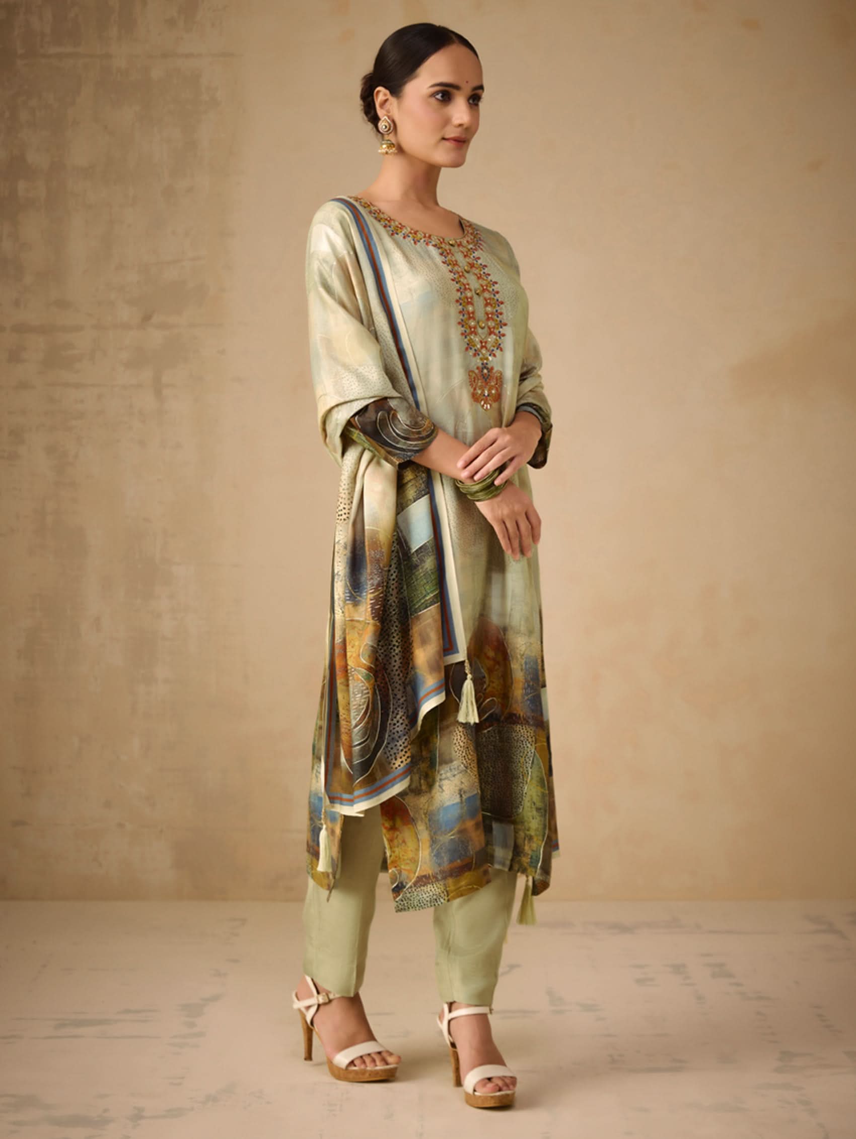 Woman wearing a traditional outfit with a patterned dupatta against a beige background