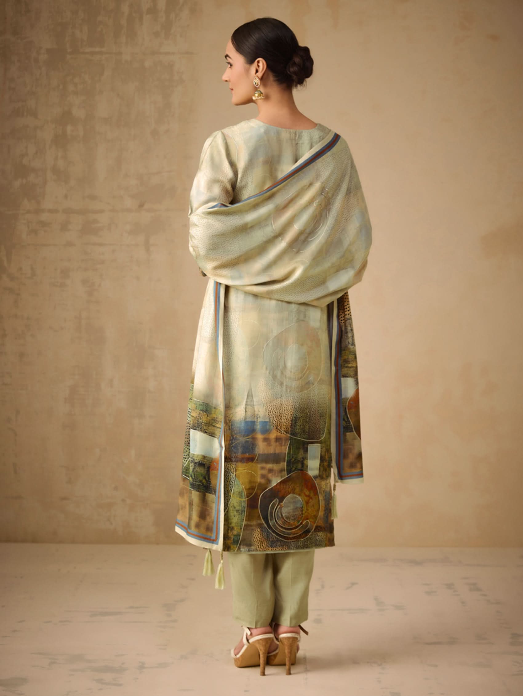 Woman wearing a traditional outfit with a patterned dupatta against a beige background