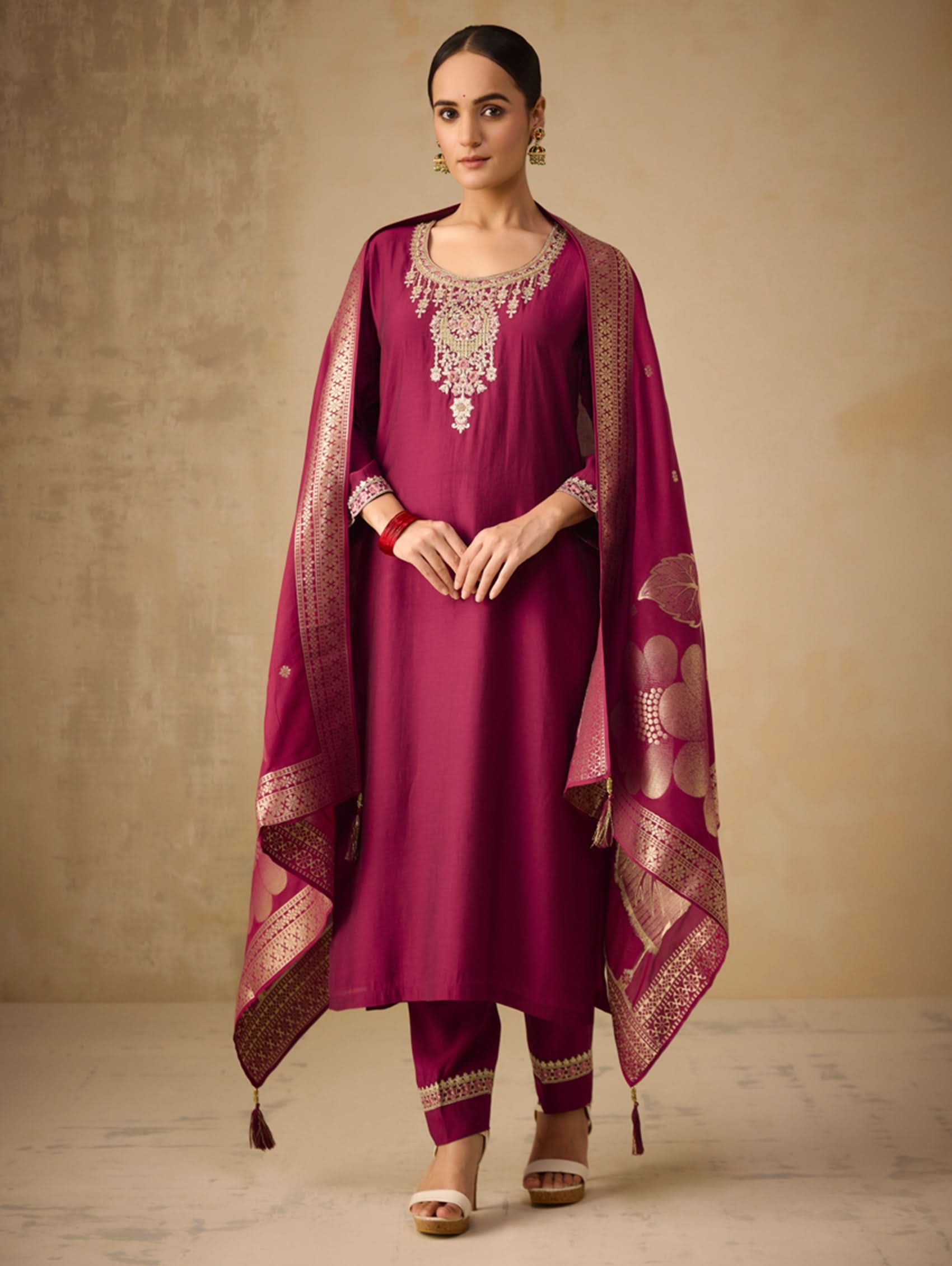 Woman wearing a magenta traditional outfit with a matching dupatta on a beige background