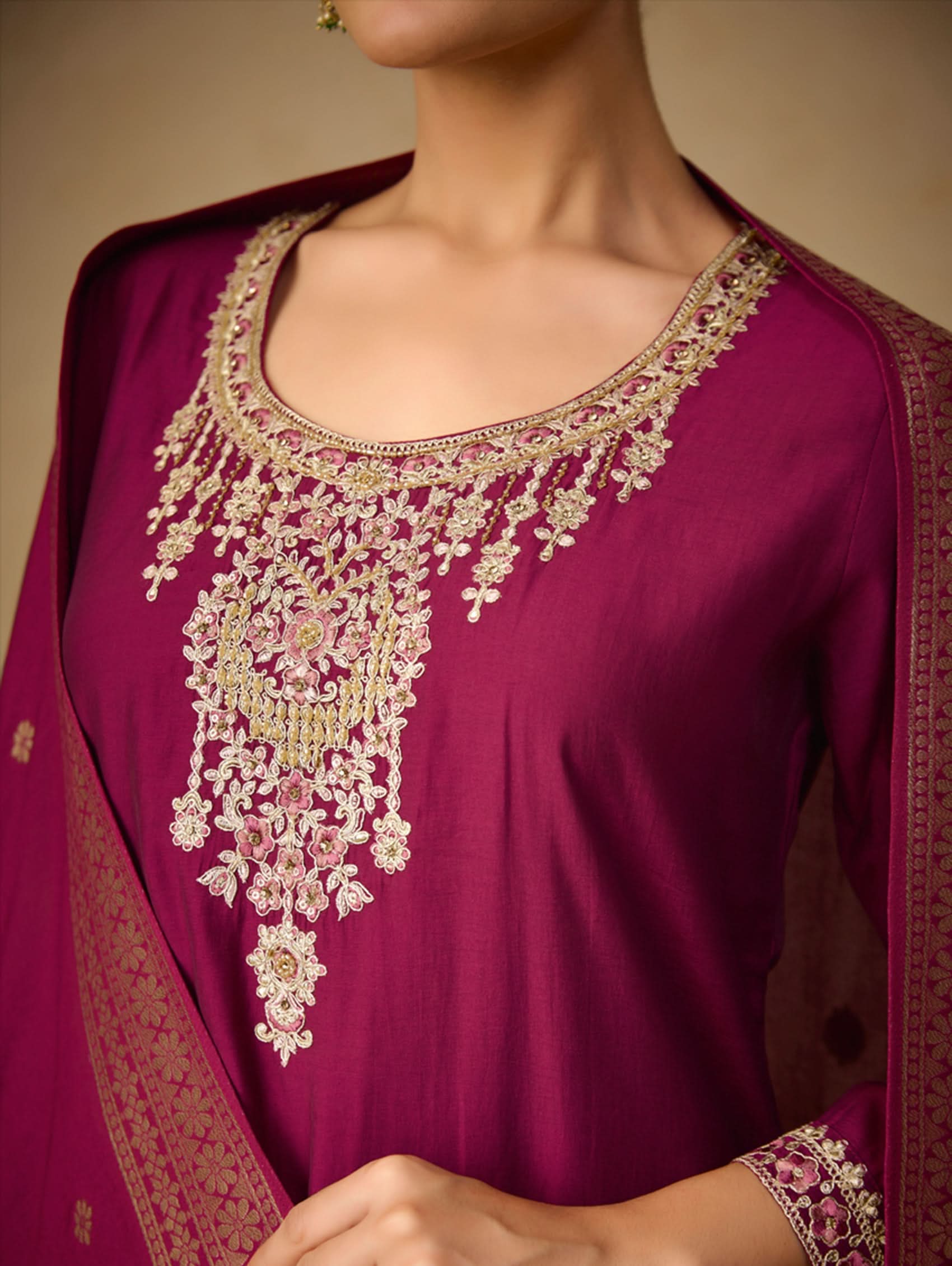 Close-up of a magenta embroidered traditional outfit with gold detailing.