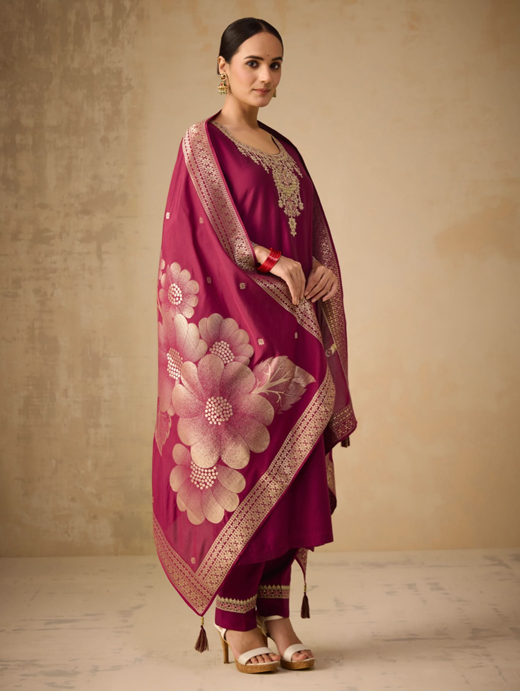 Woman wearing a magenta traditional outfit with floral design against a beige background