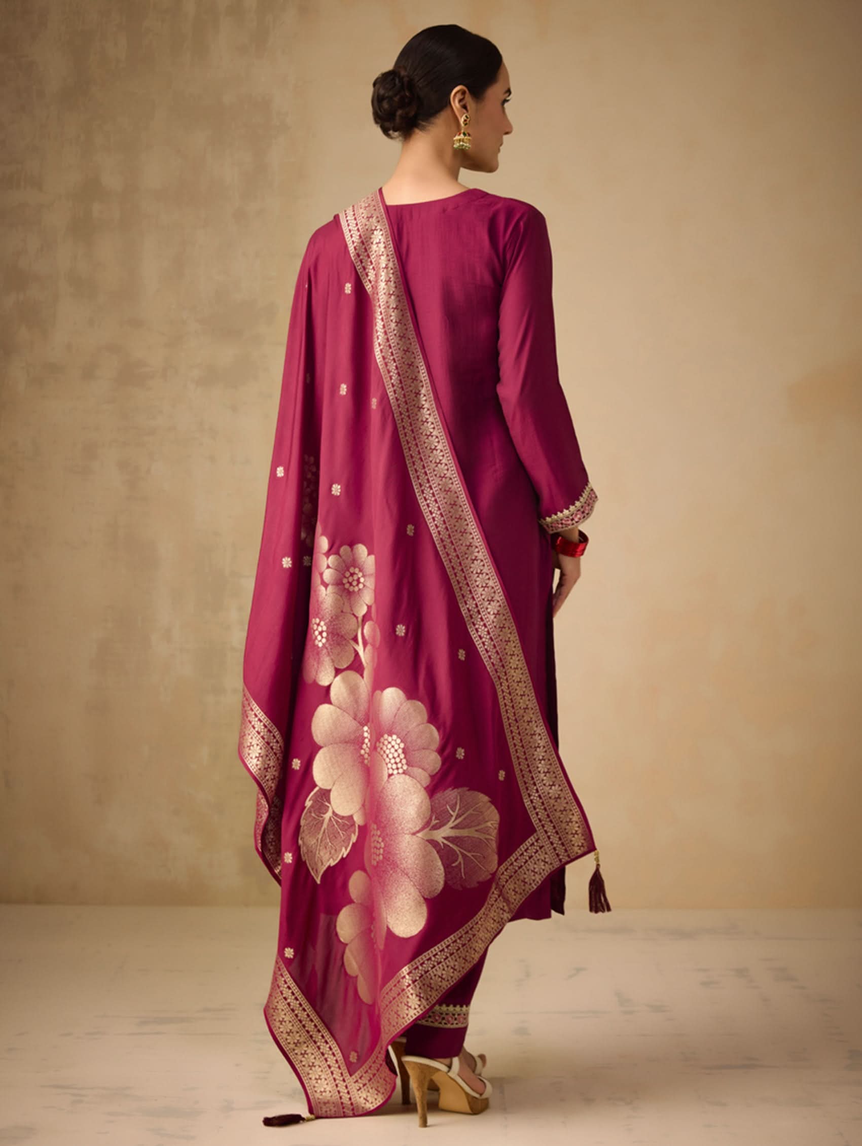 Woman wearing a magenta traditional outfit with floral patterns on a beige background