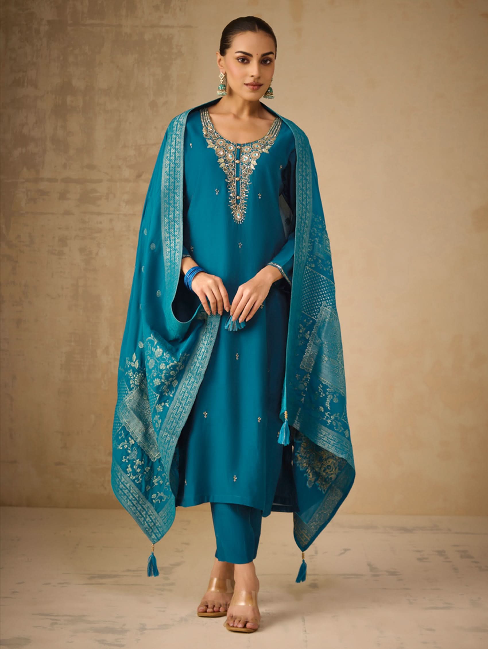 Woman wearing a teal traditional outfit with a matching dupatta against a beige background