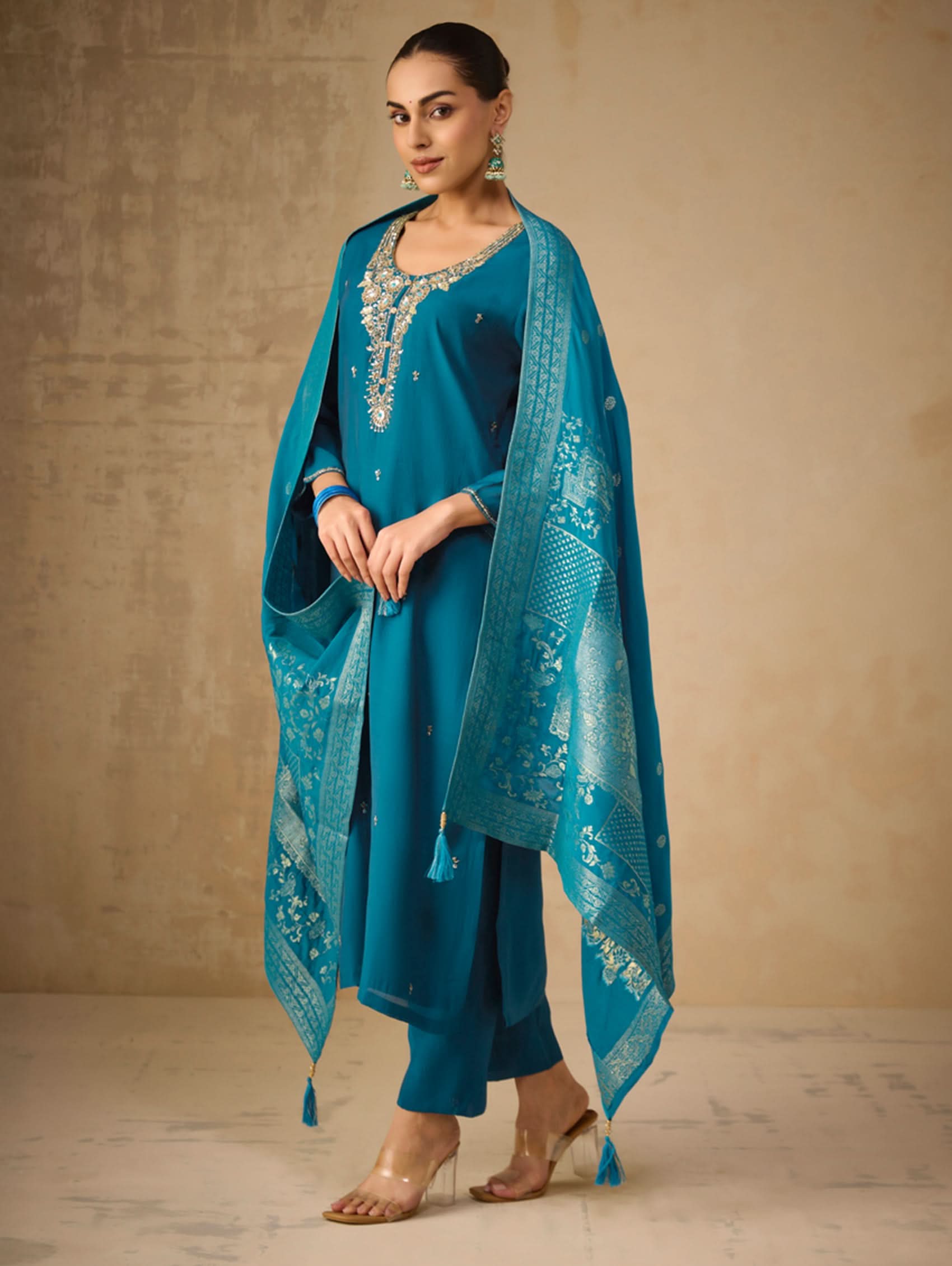 Woman wearing a teal traditional outfit with a matching dupatta against a beige background