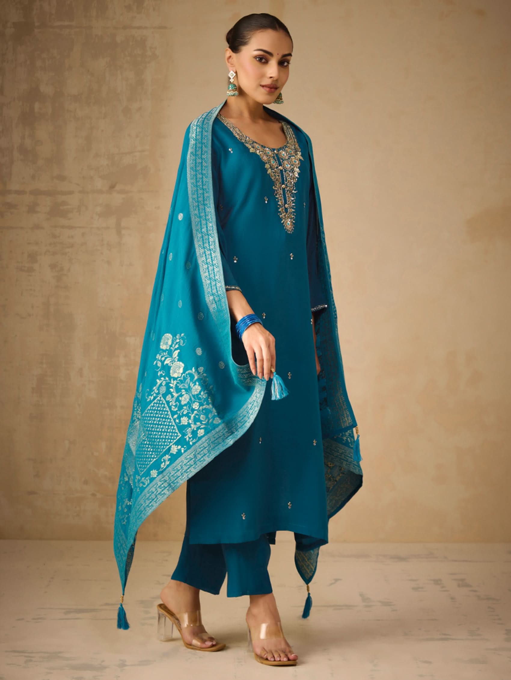 Woman wearing a teal traditional outfit with a matching dupatta against a beige background