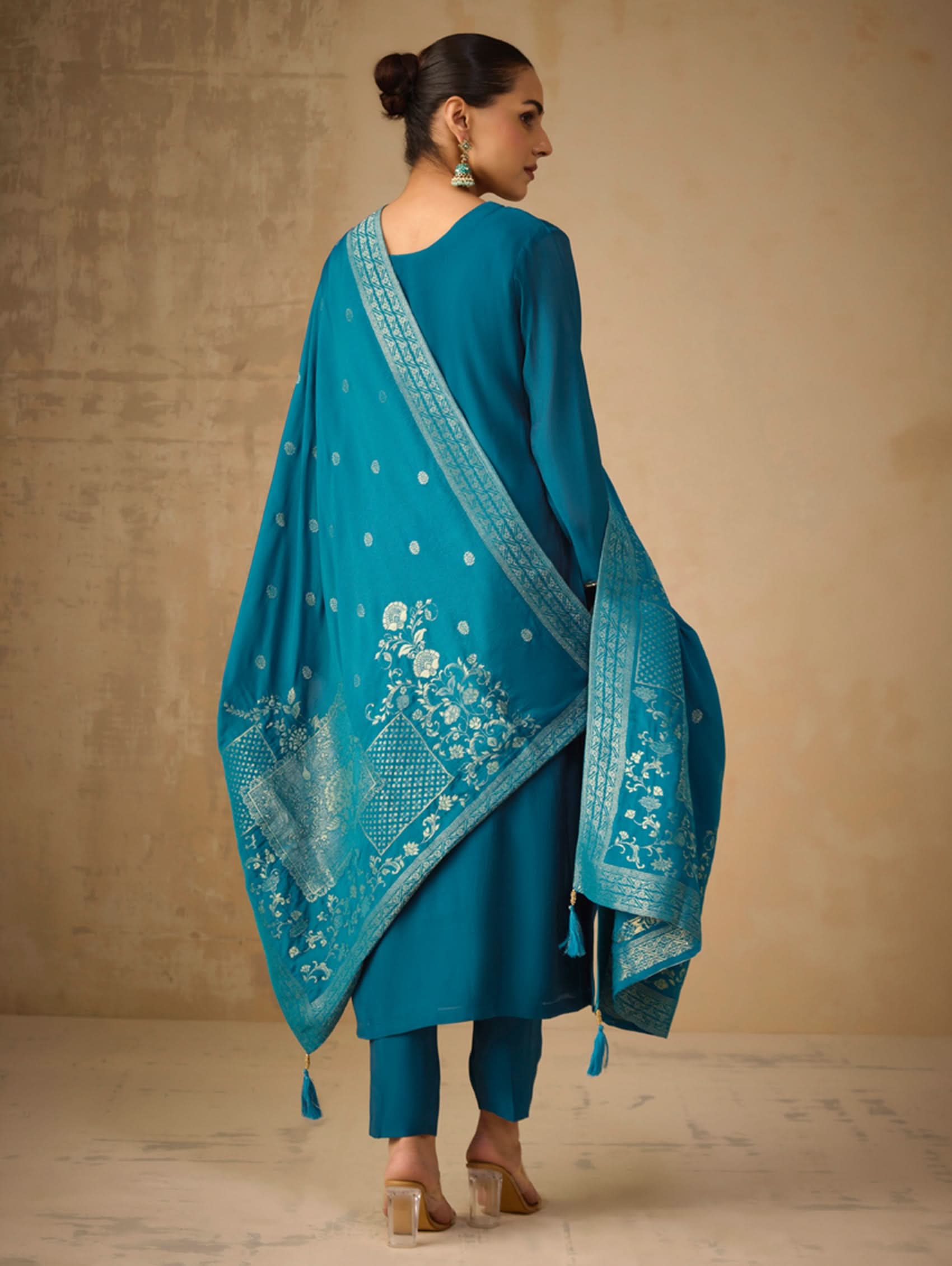 Woman wearing a turquoise traditional outfit with a matching dupatta against a beige background