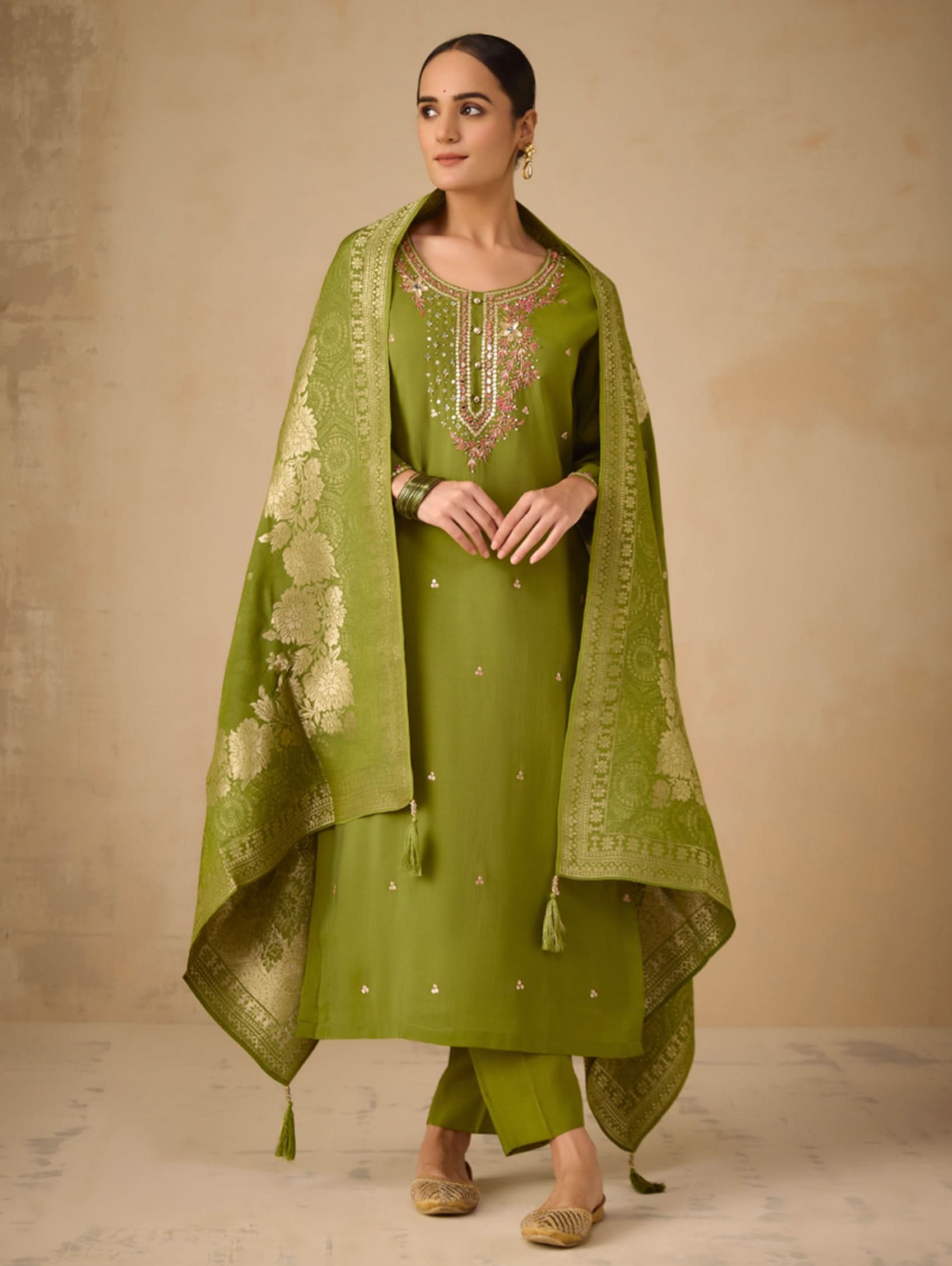 Woman wearing a green traditional outfit with a matching dupatta against a beige background