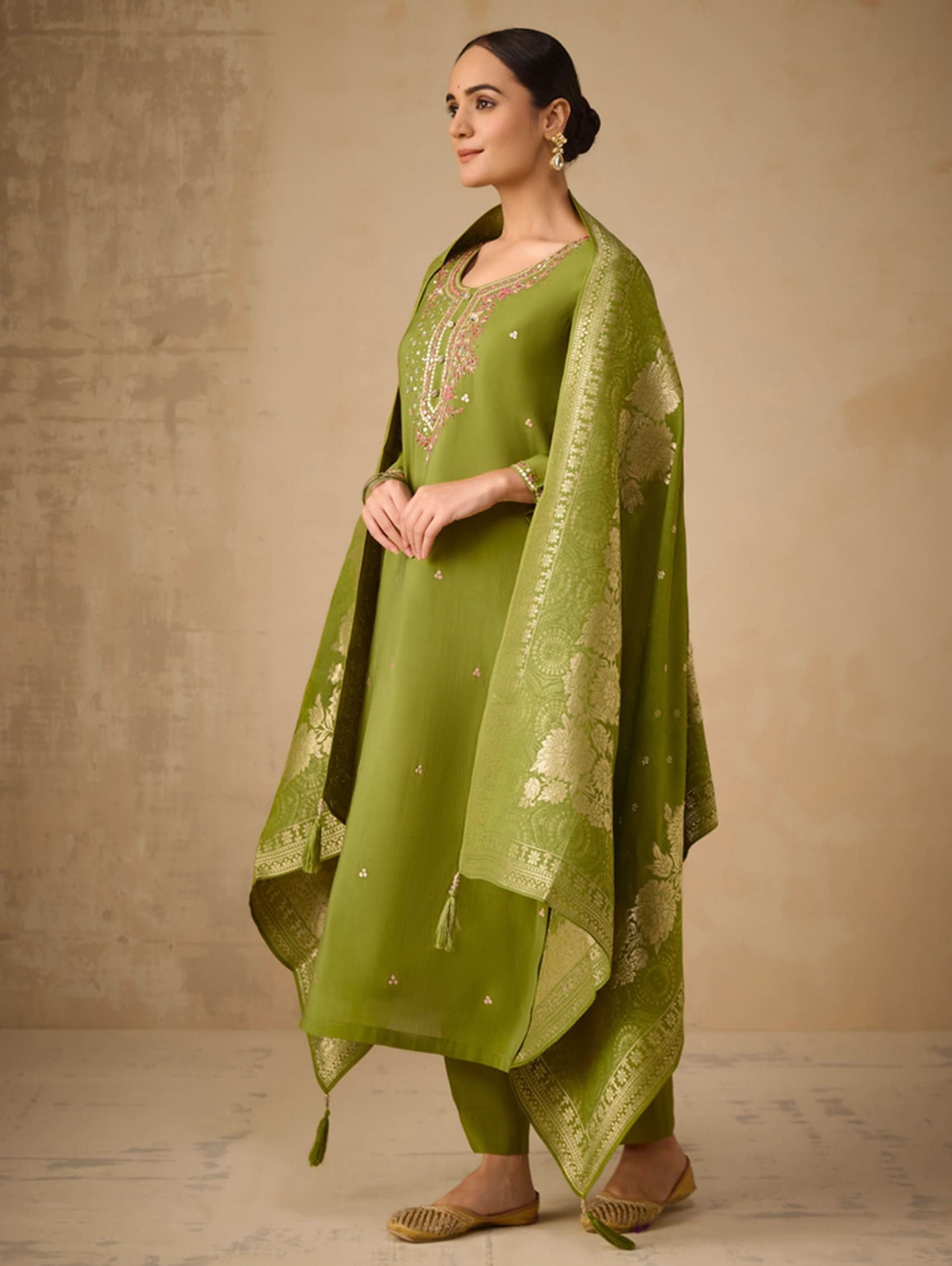 Woman wearing a green traditional outfit with a matching dupatta against a beige background
