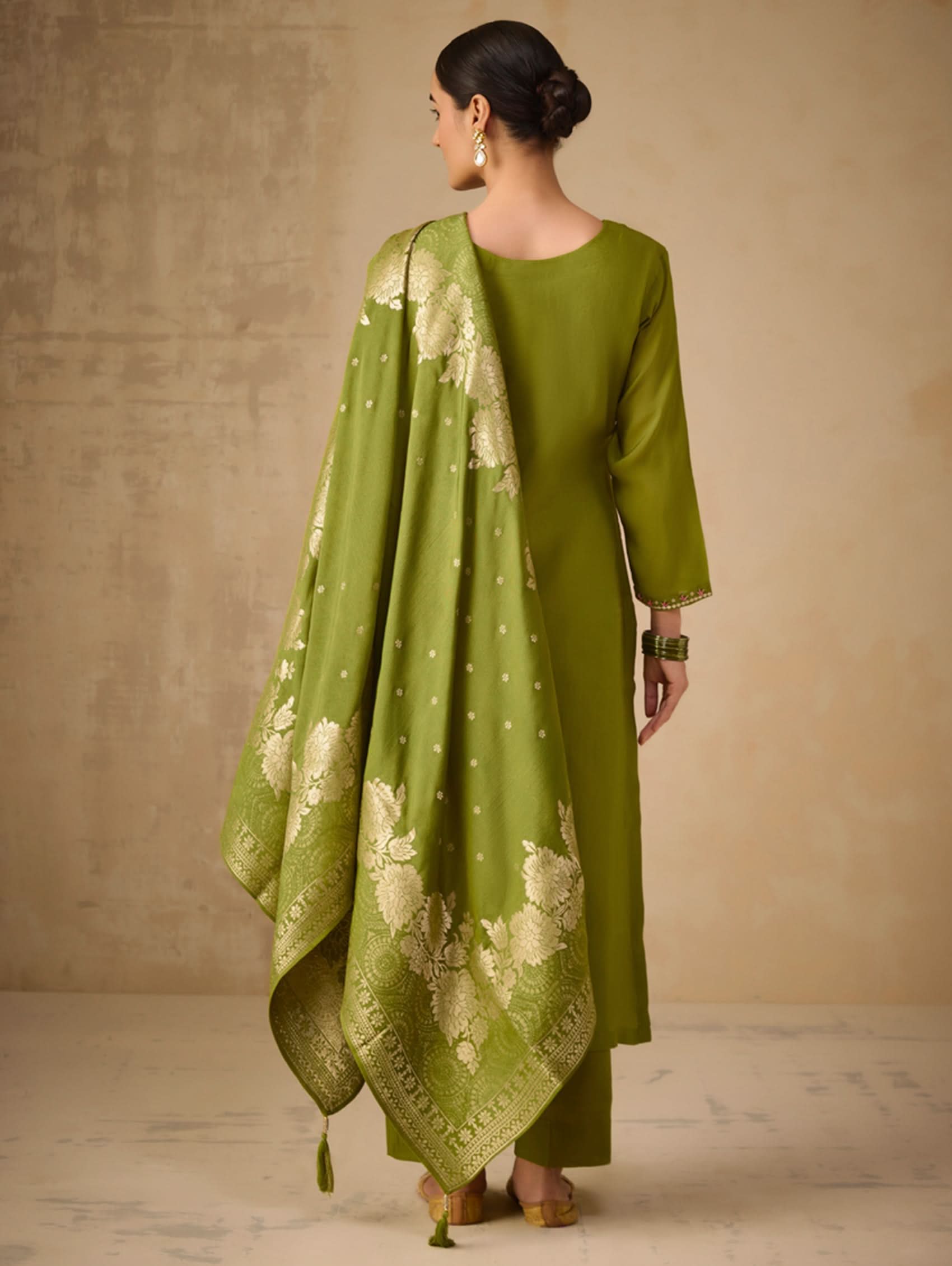Woman wearing a green traditional outfit with a matching dupatta against a beige background