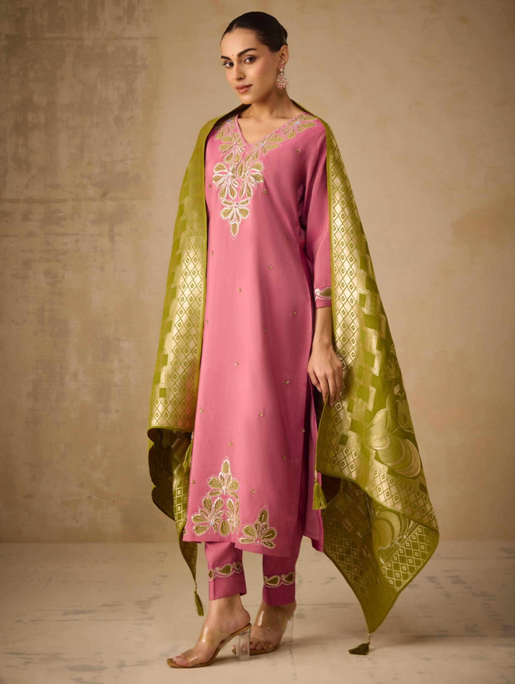 Woman wearing a pink outfit with green dupatta against a beige background
