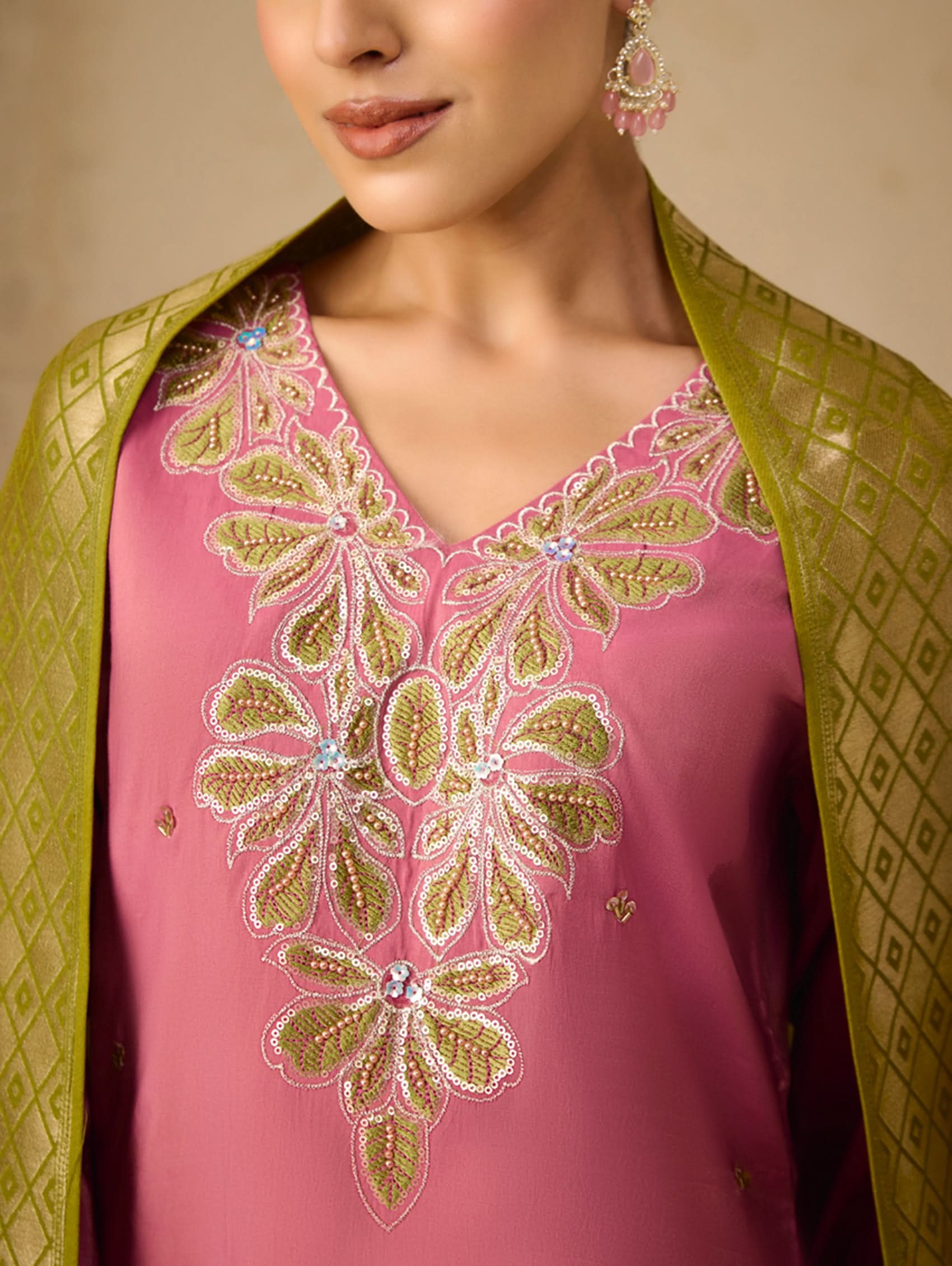 Close-up of a pink embroidered garment with green border on a neutral background