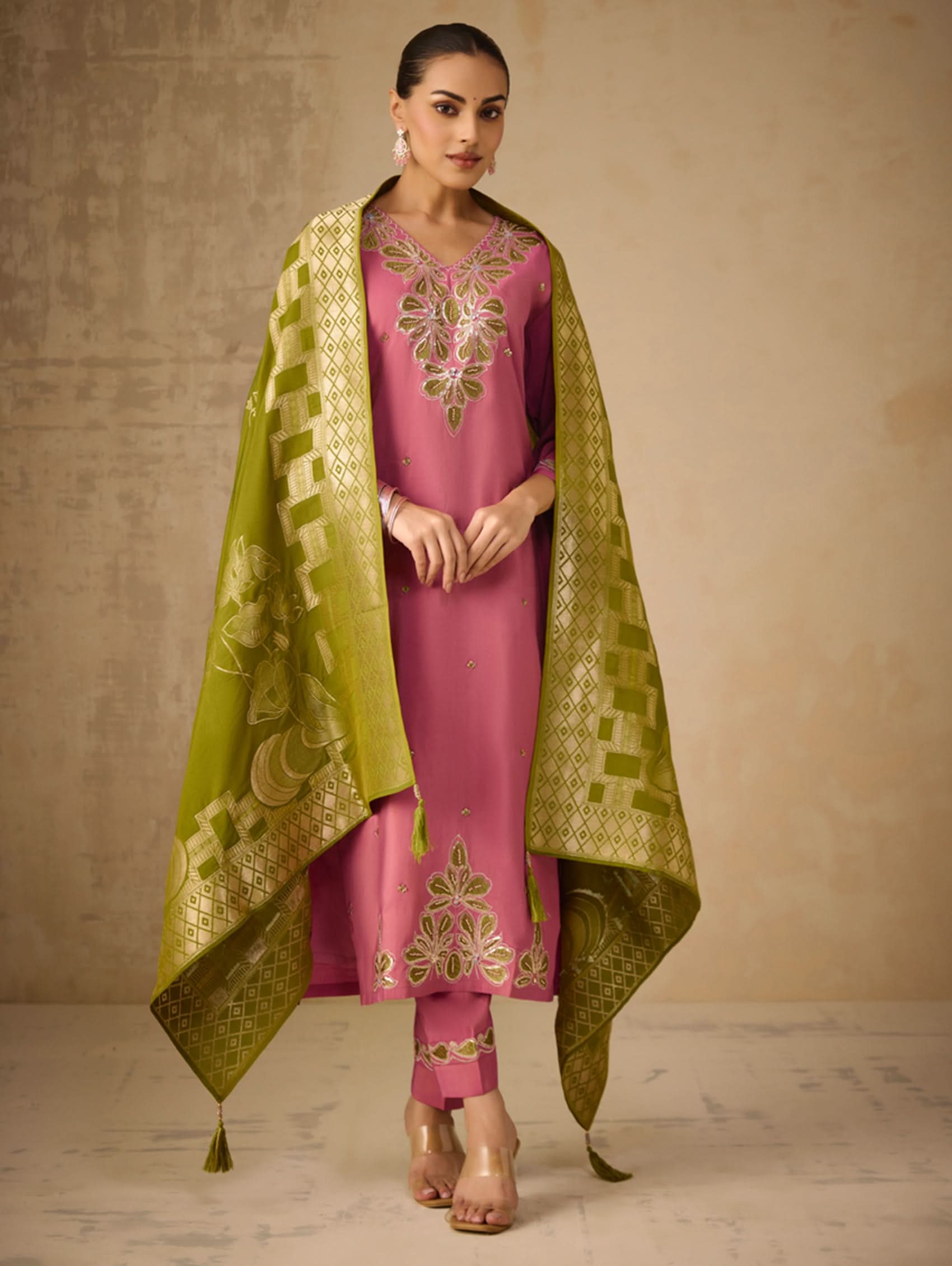 Woman wearing a pink traditional outfit with a green dupatta against a beige background