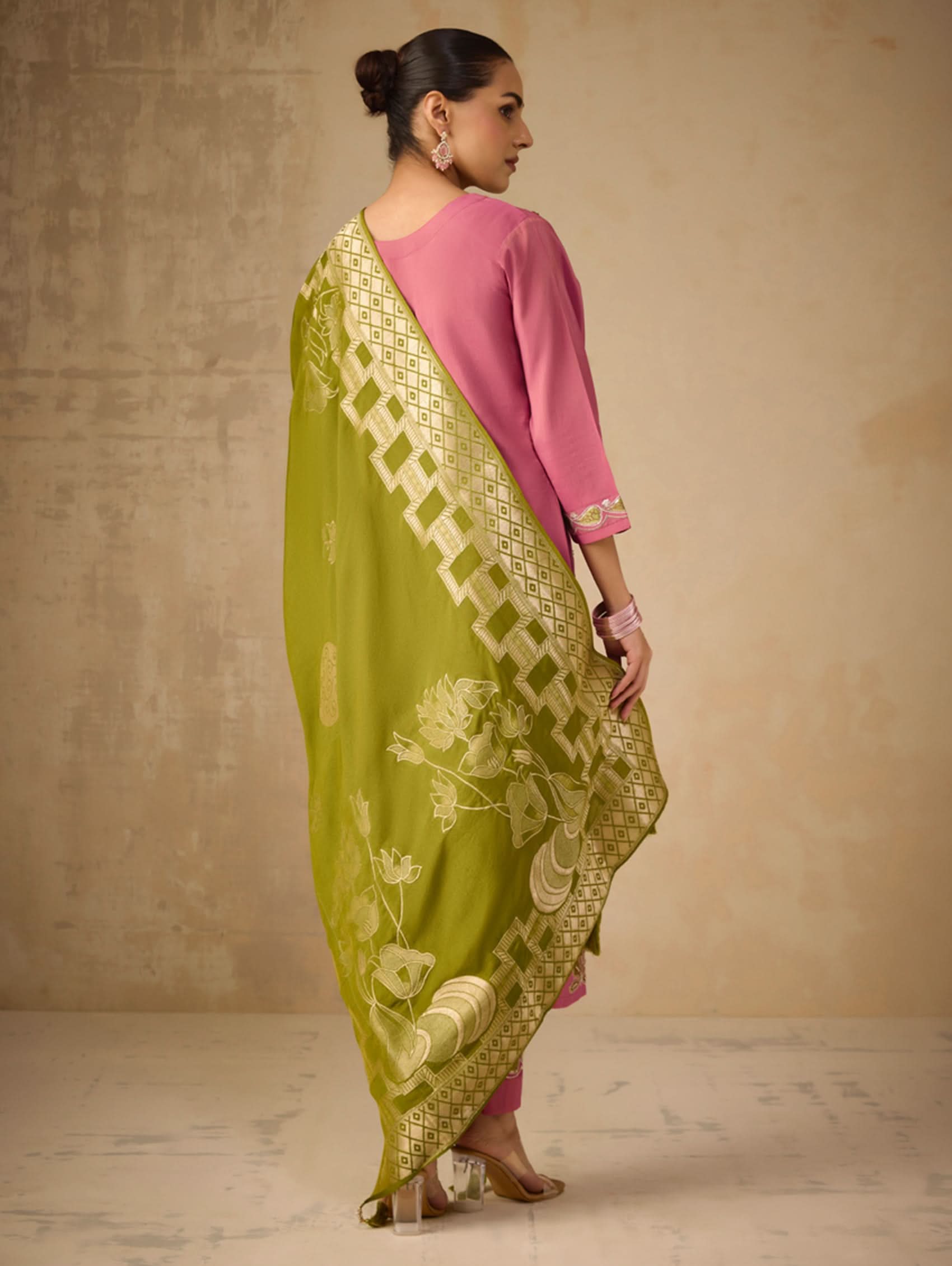 Woman wearing a pink outfit with a green saree against a beige background