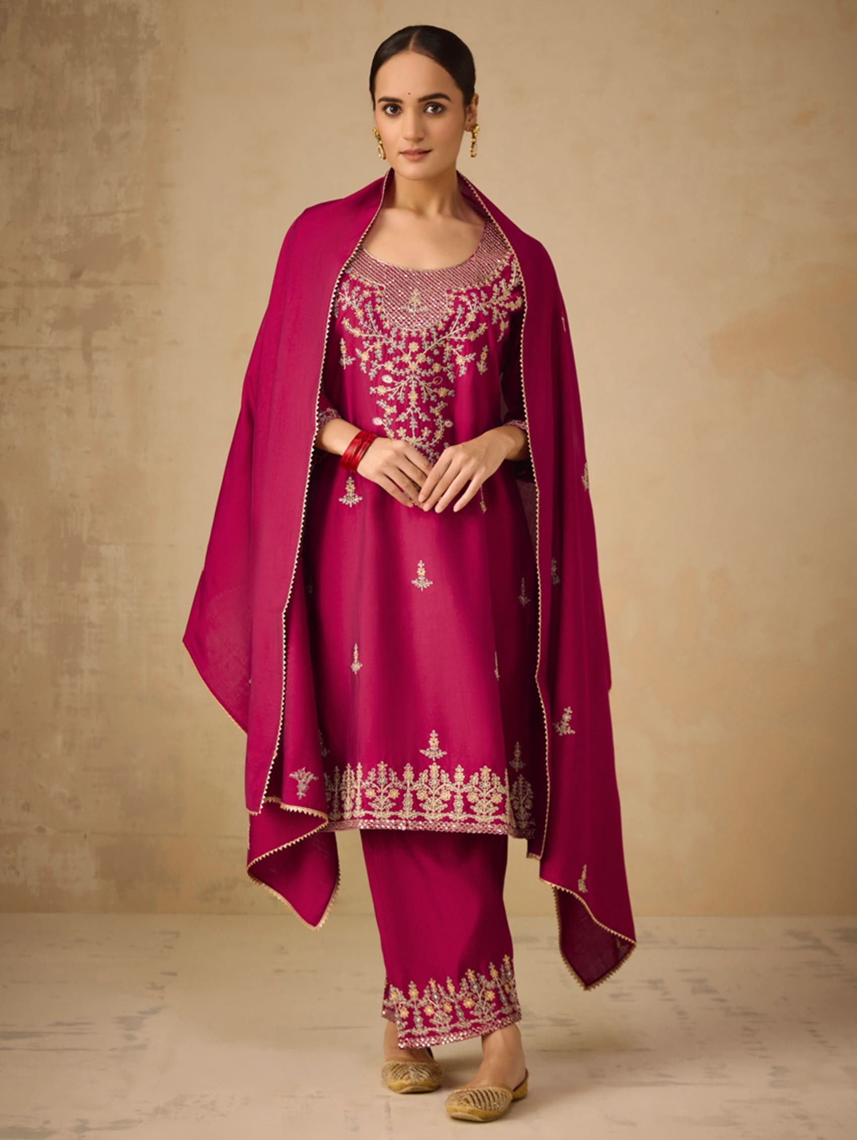 Woman wearing a magenta traditional outfit with intricate embroidery on a beige background