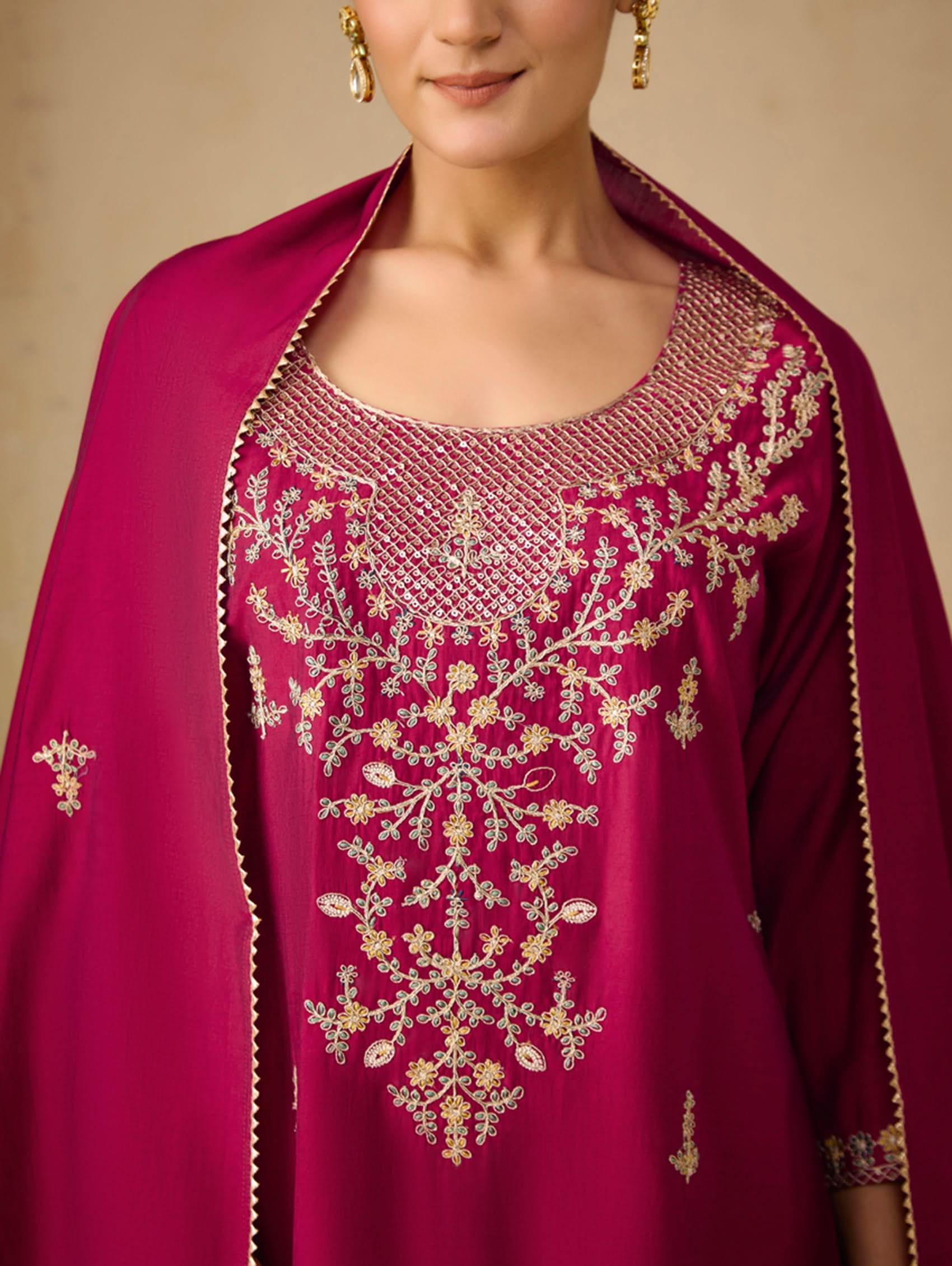 Close-up of a person wearing a pink embroidered traditional outfit with a beige background
