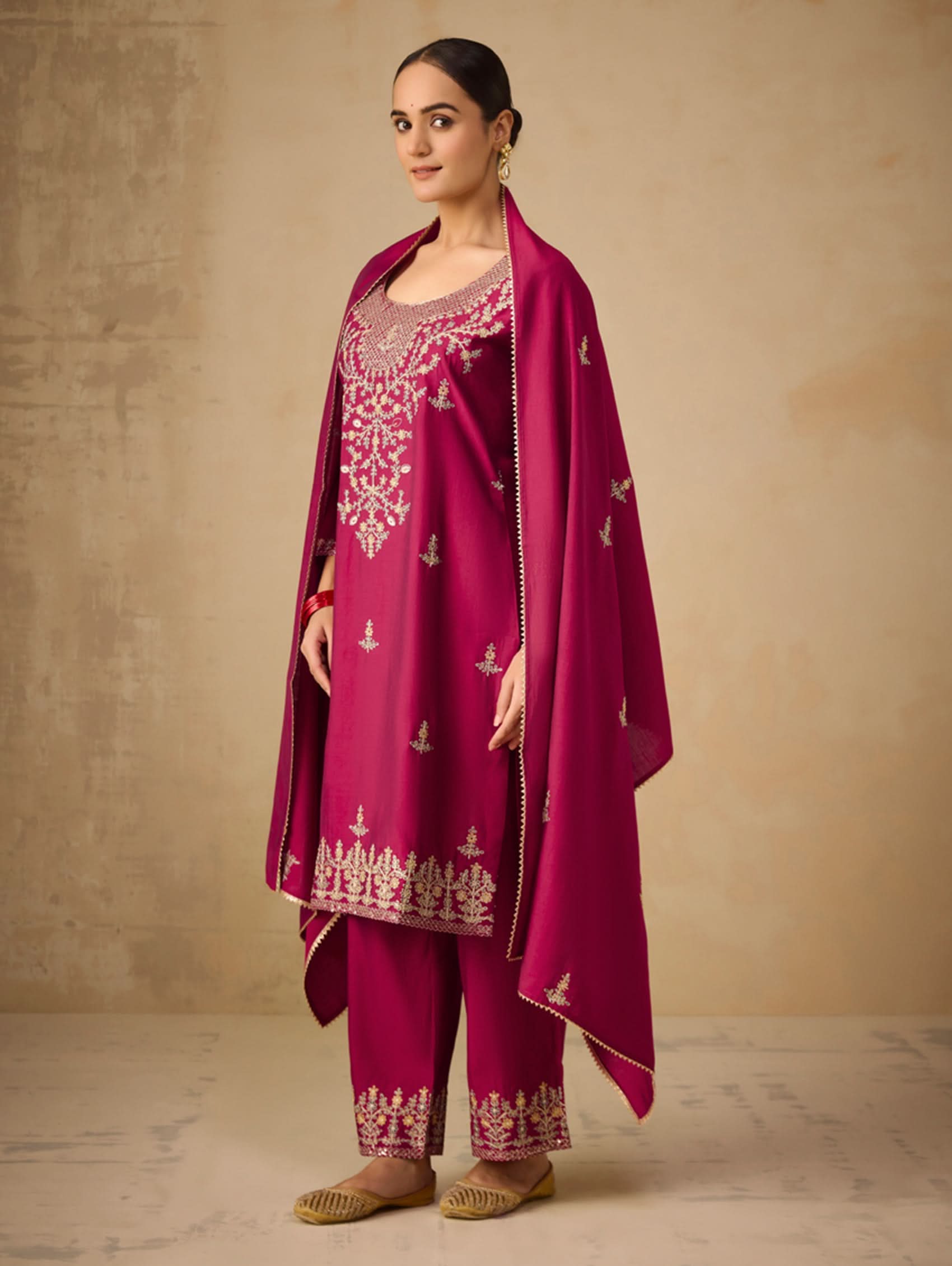 Woman wearing a magenta embroidered traditional outfit against a beige background