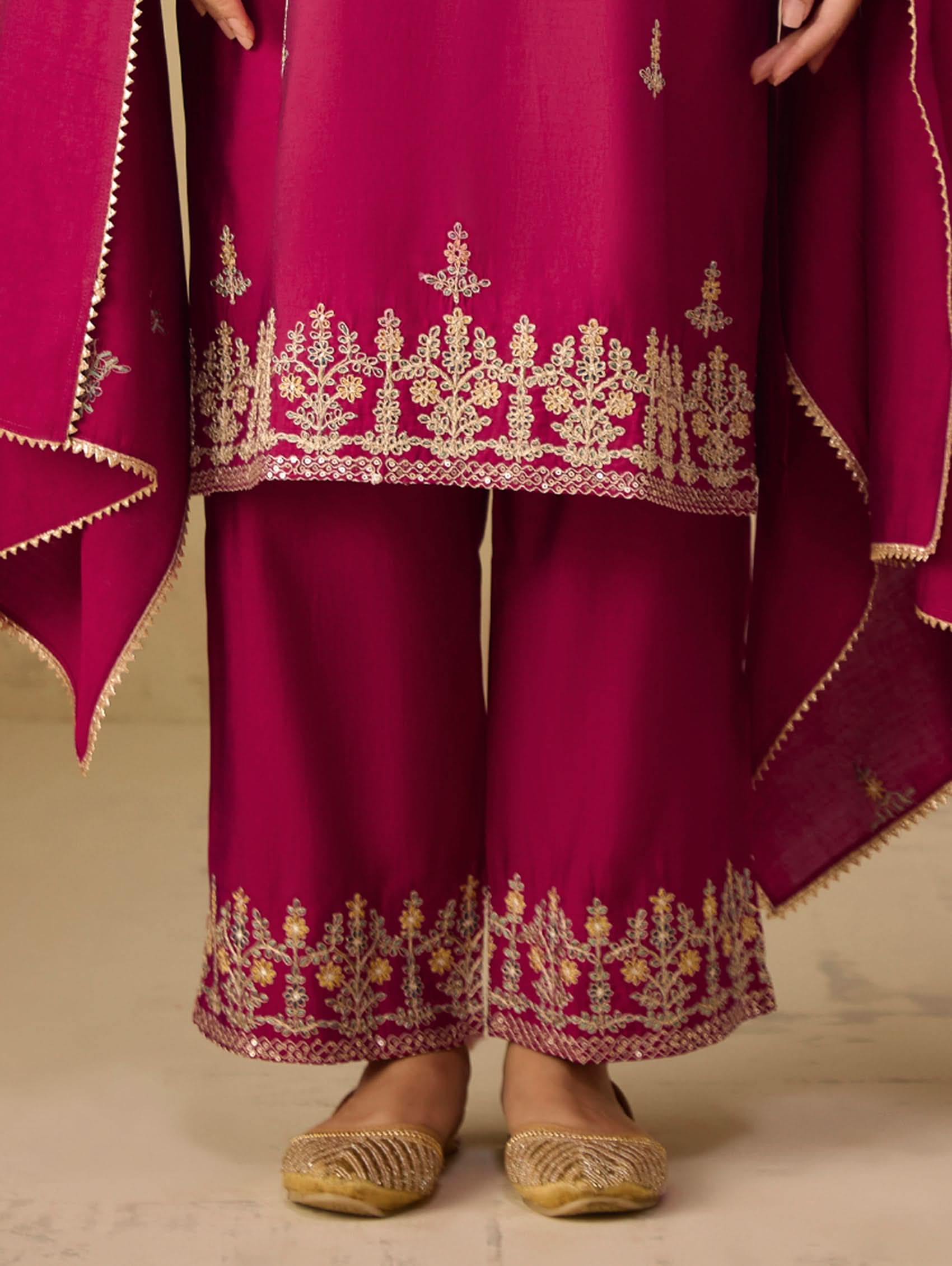 Maroon traditional outfit with gold embroidery on a neutral background