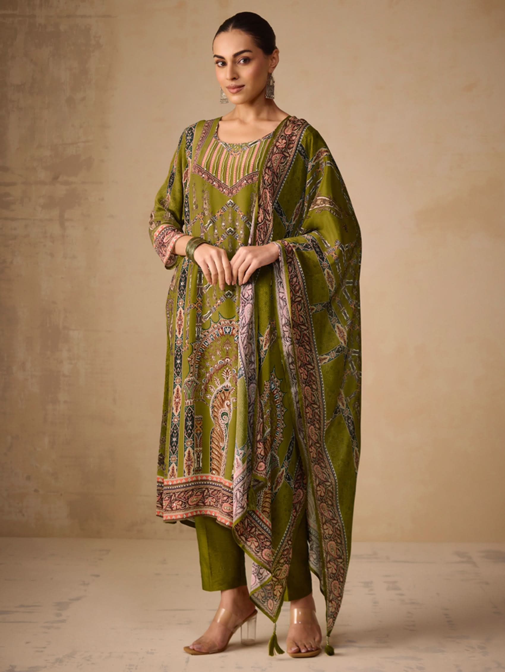 Woman wearing a green traditional outfit with a patterned dupatta against a beige background