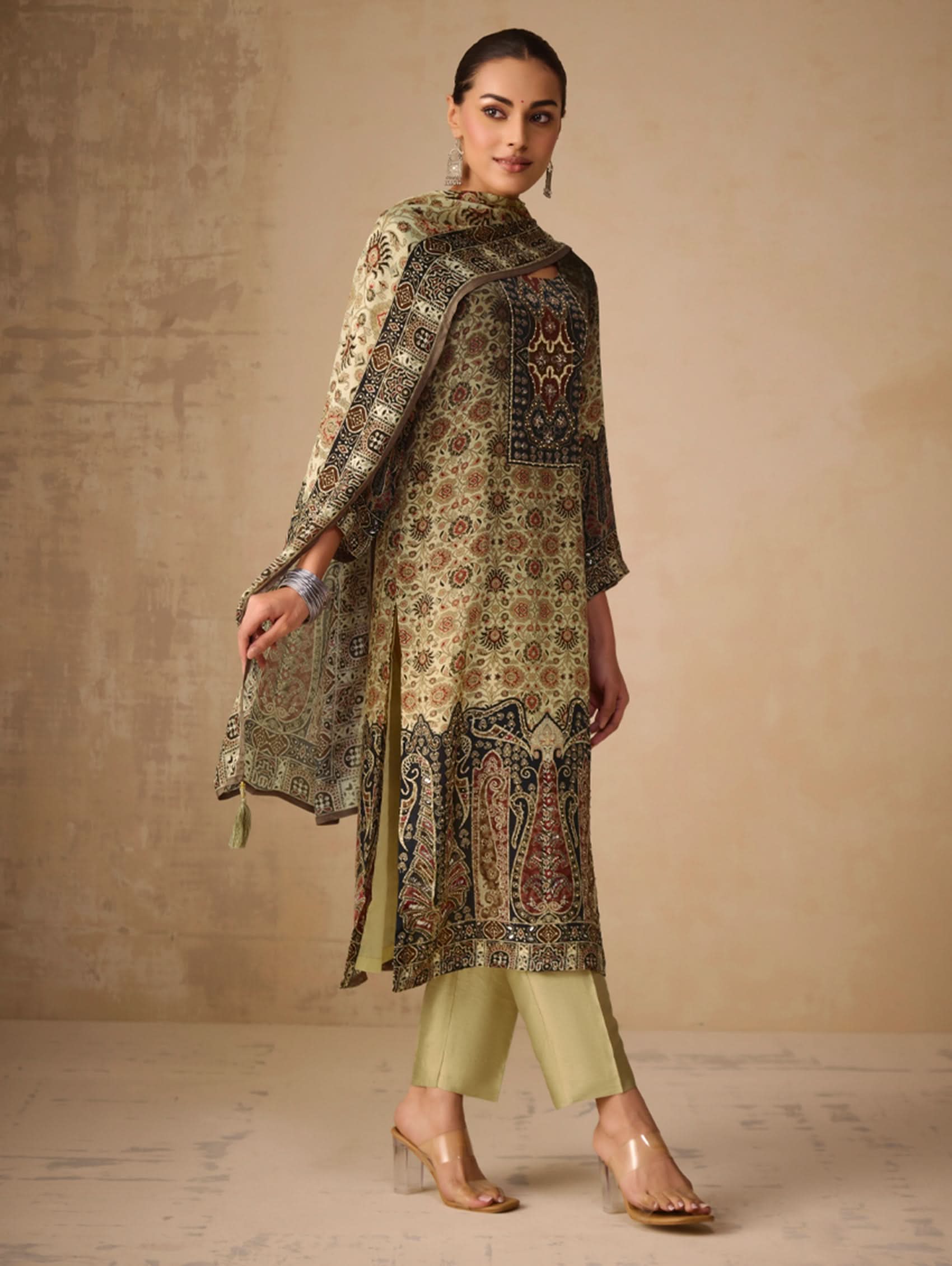 Woman wearing a traditional outfit with a patterned shawl and dress against a beige background