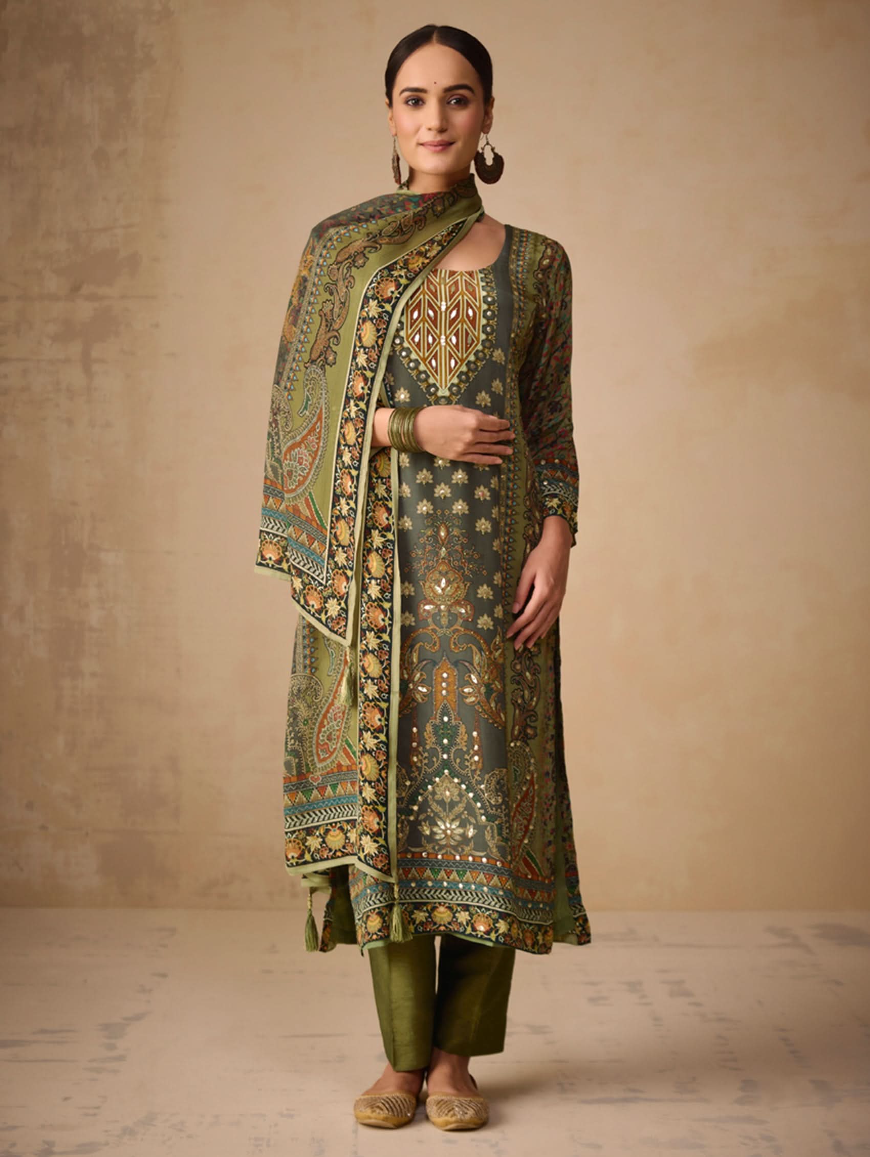 Woman wearing a traditional green and gold outfit with a matching dupatta against a beige background