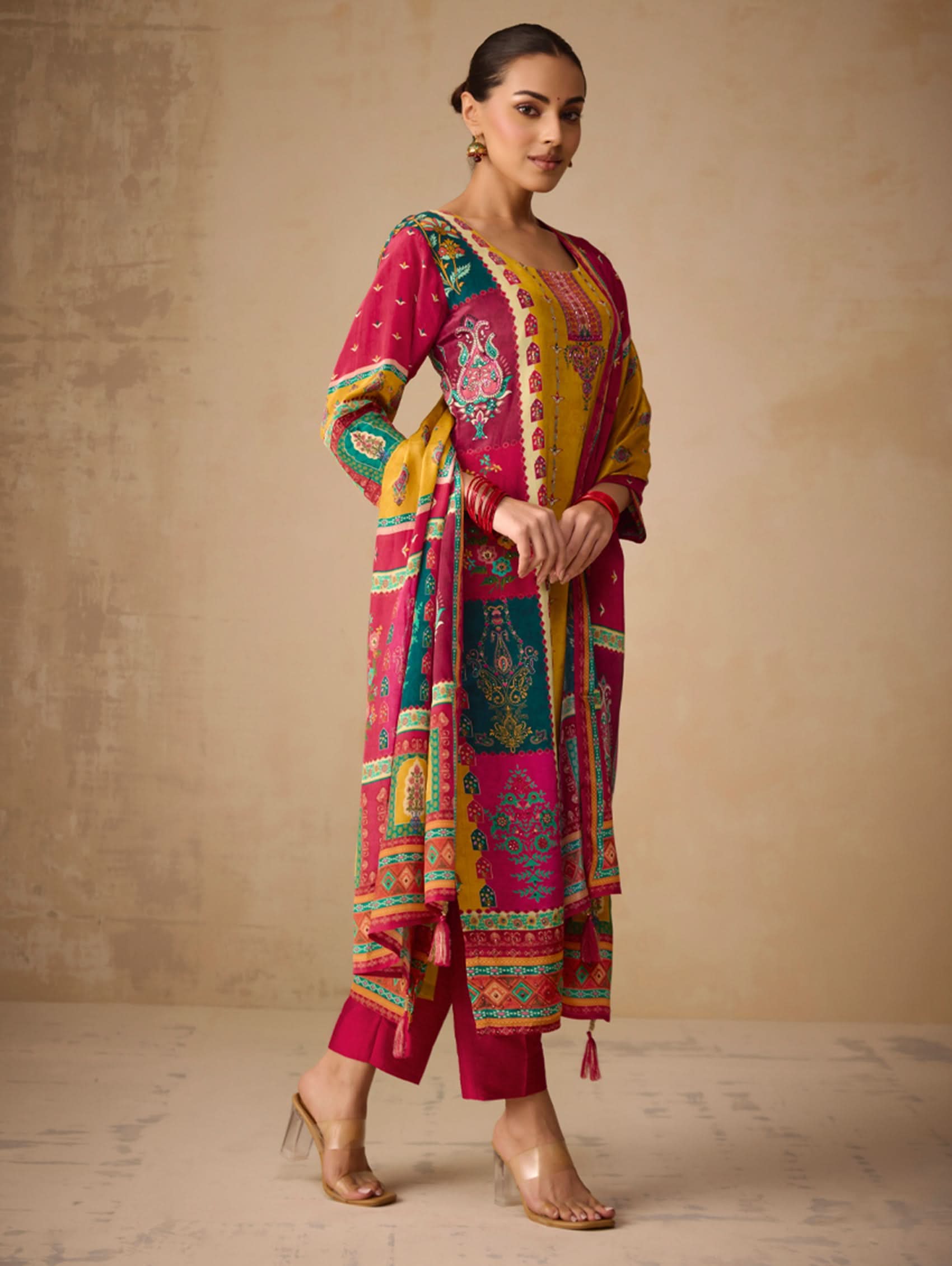 Woman wearing a colorful traditional outfit with a patterned dupatta against a beige background