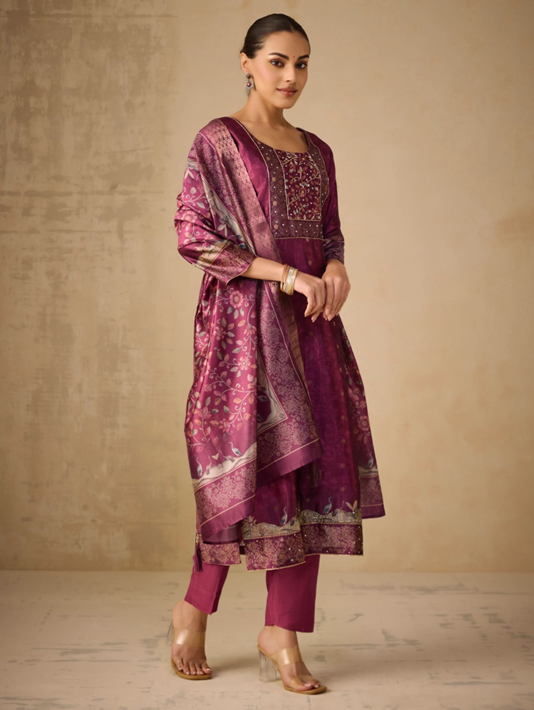 Woman wearing a traditional outfit with a purple and pink patterned dress against a beige background