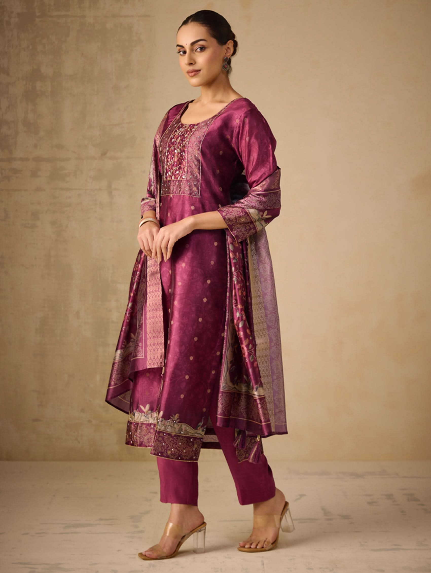 Woman wearing a traditional purple outfit with intricate patterns against a neutral background