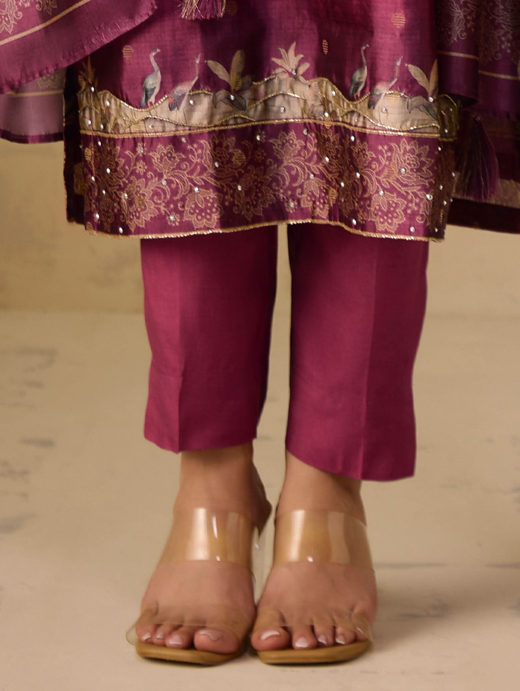 Purple traditional outfit with embroidered top and pants, worn with transparent sandals on a neutral background.