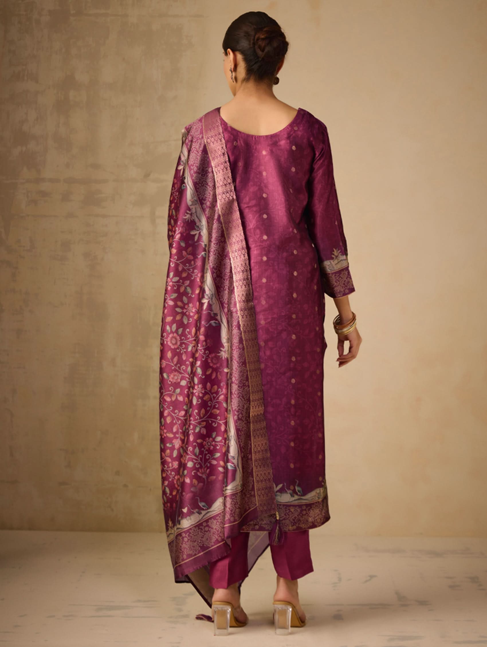 Woman wearing a traditional outfit with a pink kurta and pants against a beige background