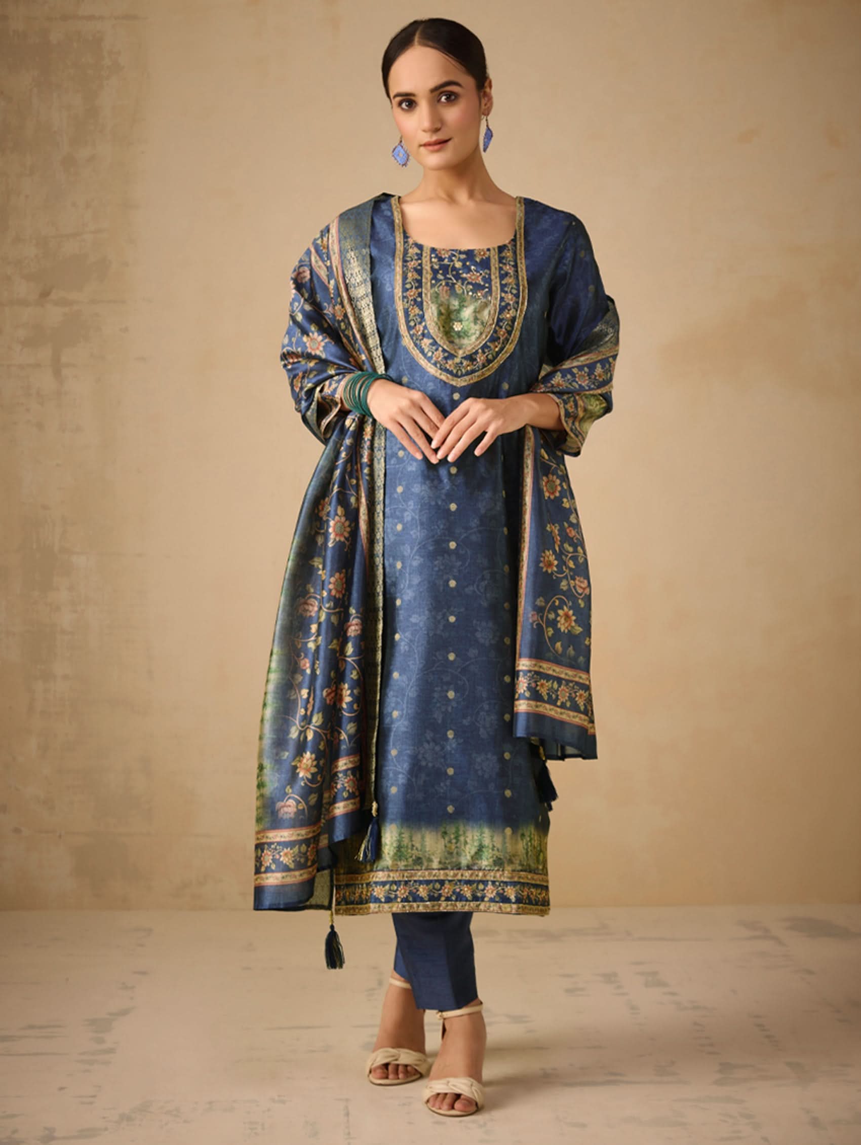 Woman wearing a blue embroidered traditional outfit with a beige background