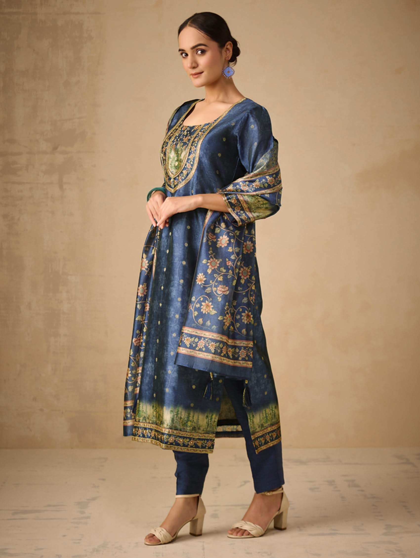 Woman wearing a blue embroidered traditional outfit against a beige background