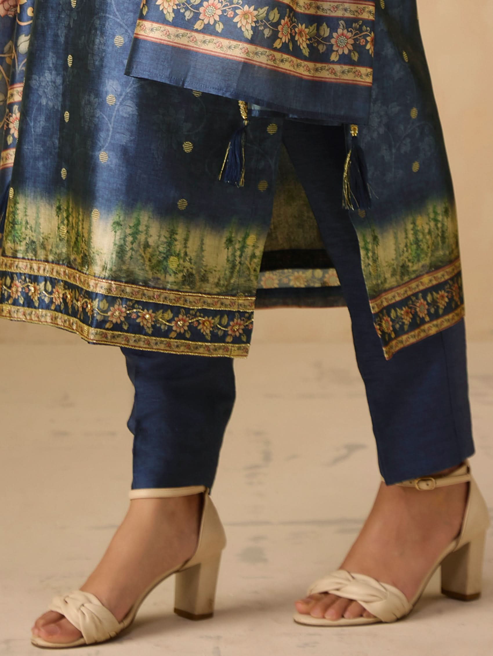 Blue embroidered traditional outfit with matching pants and sandals on a neutral background