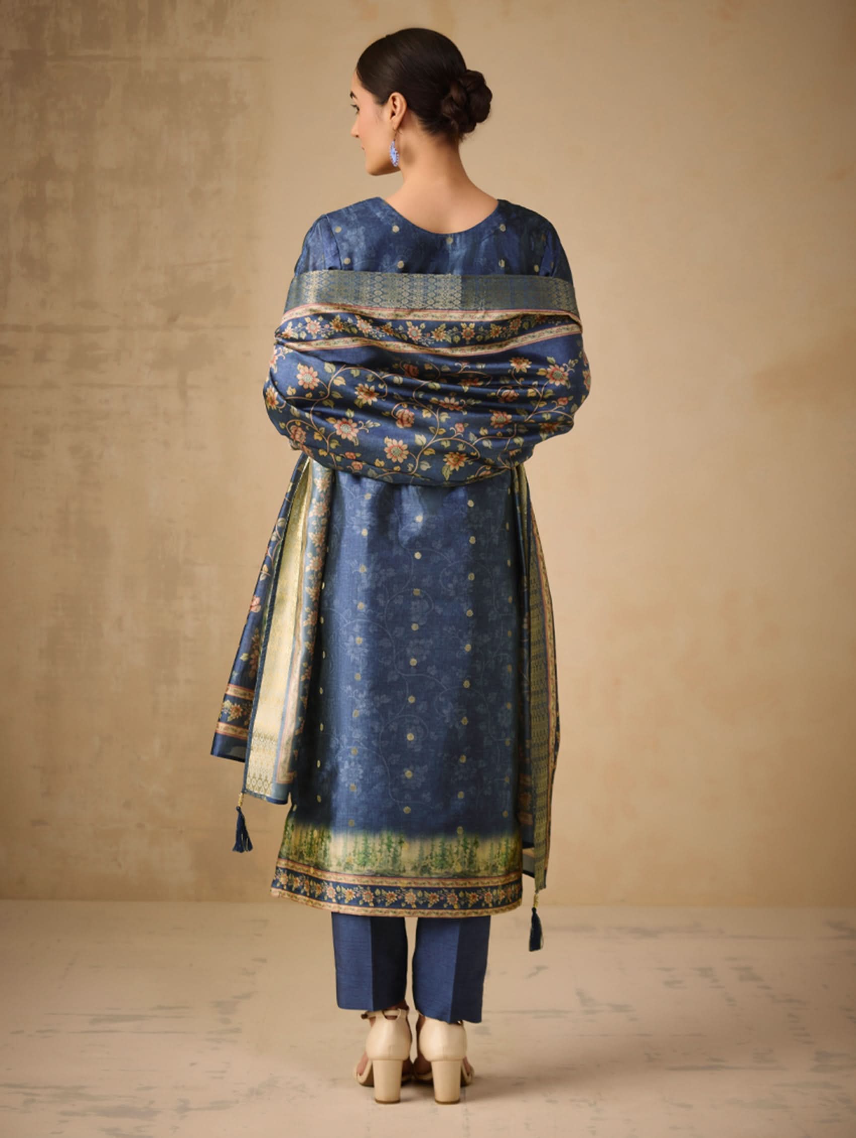 Woman wearing a blue traditional outfit with a matching dupatta against a beige background