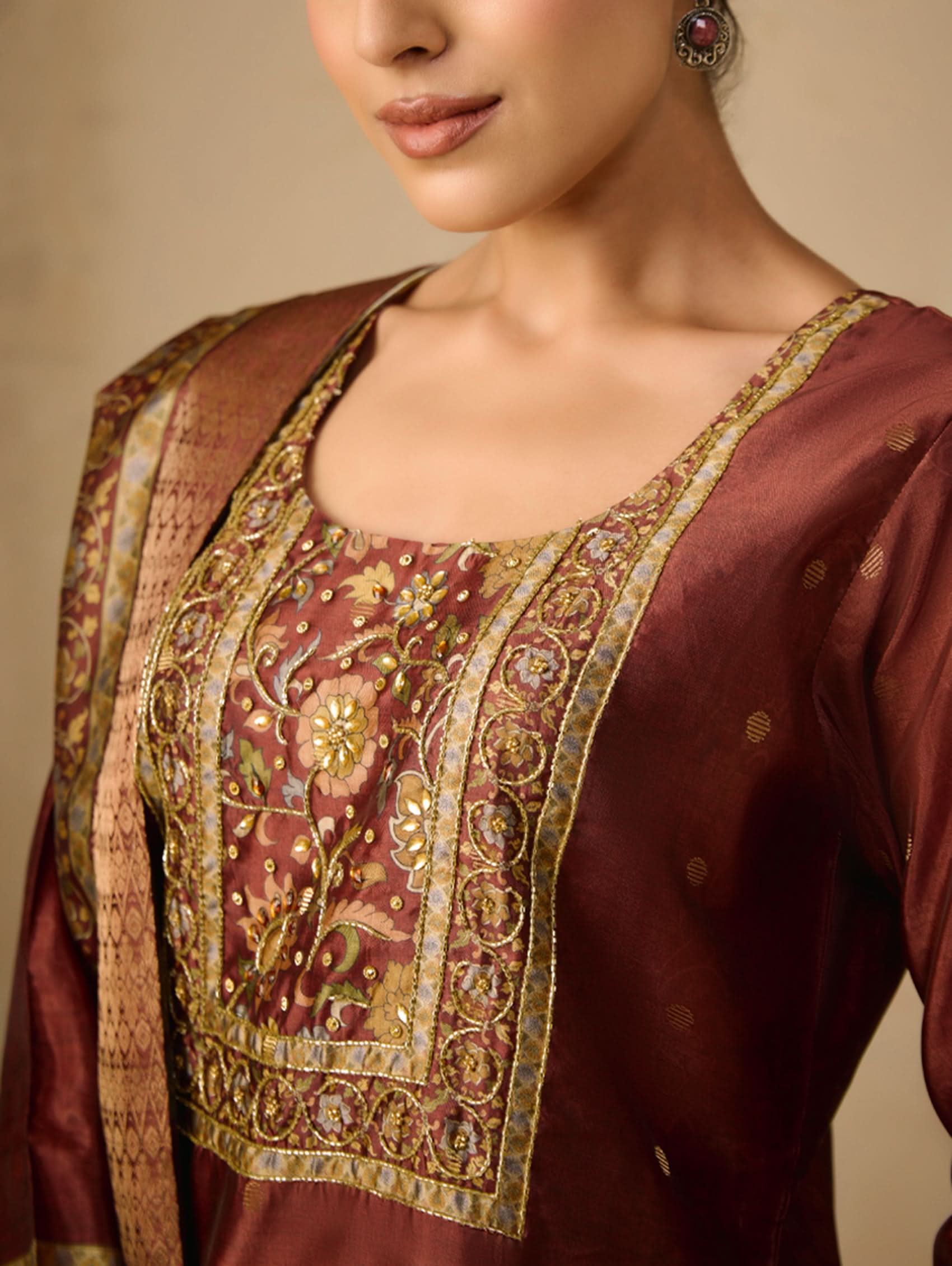 Close-up of a maroon traditional outfit with intricate gold embroidery on a beige background