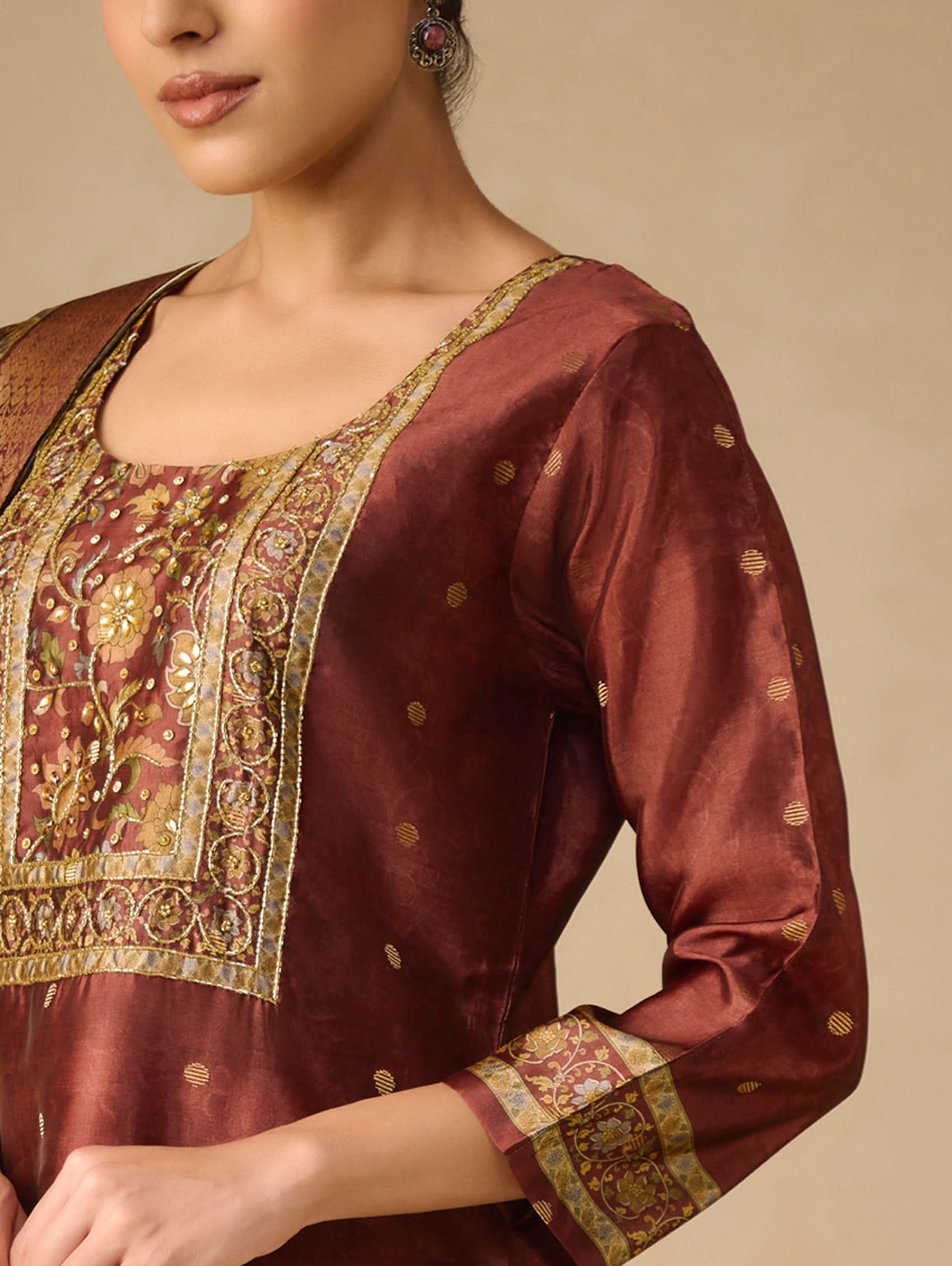 Maroon traditional outfit with gold embroidery on a beige background