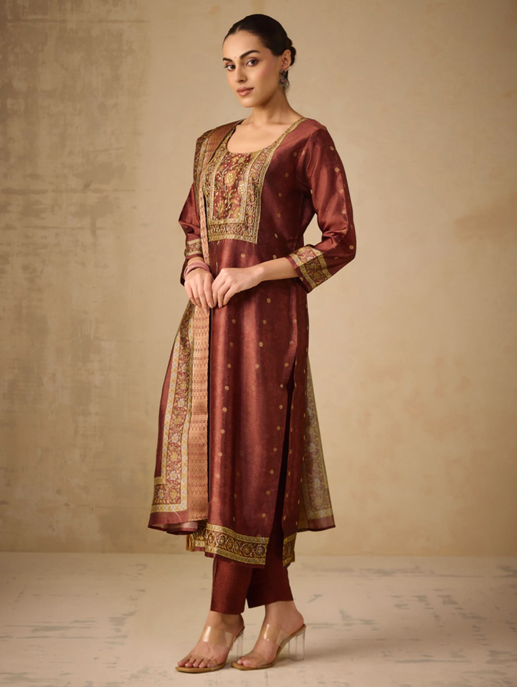 Woman wearing a traditional maroon and gold outfit against a beige background