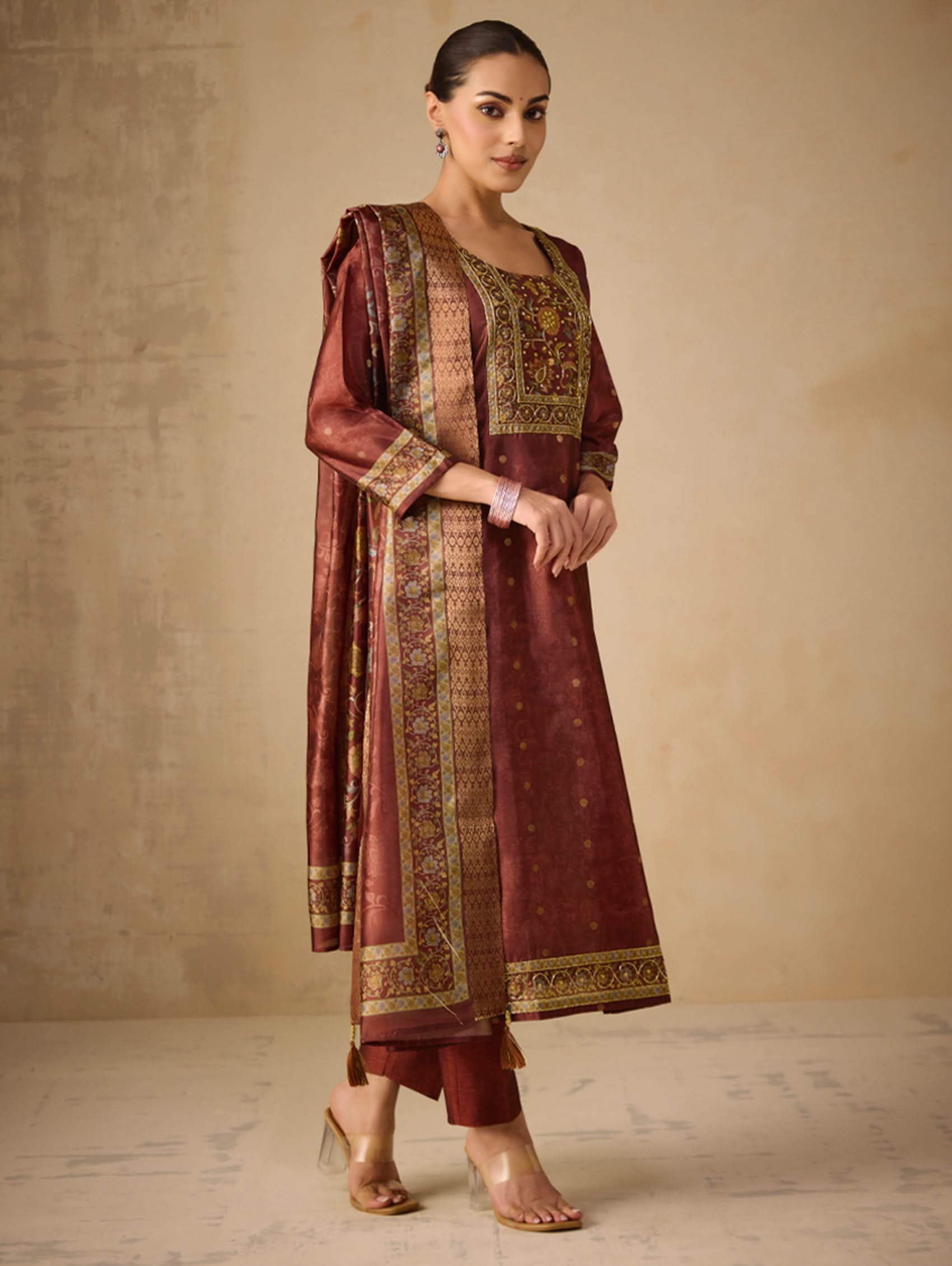 Woman wearing a traditional maroon and gold outfit with a plain background