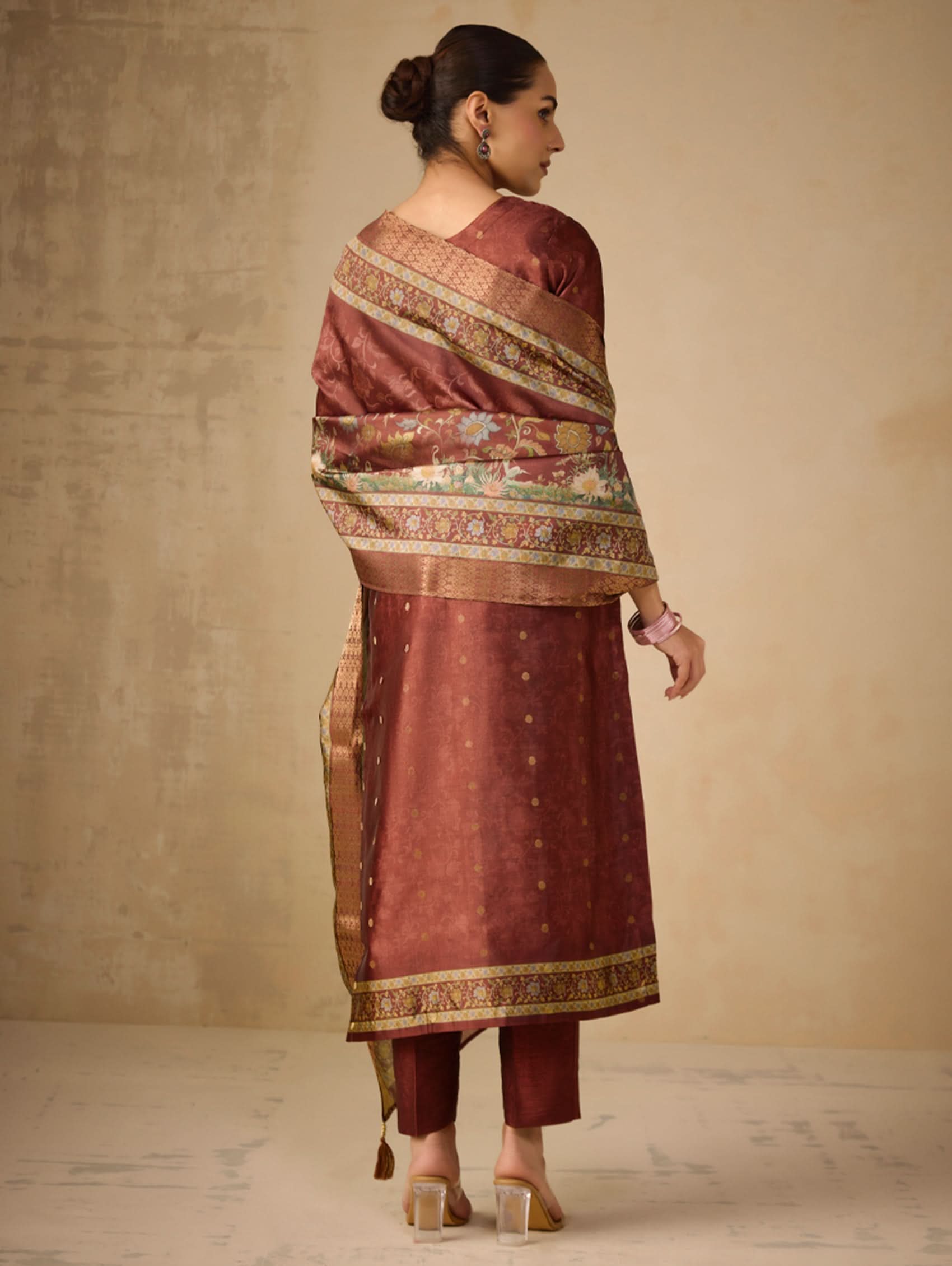 Woman wearing a traditional maroon and gold saree with a plain background