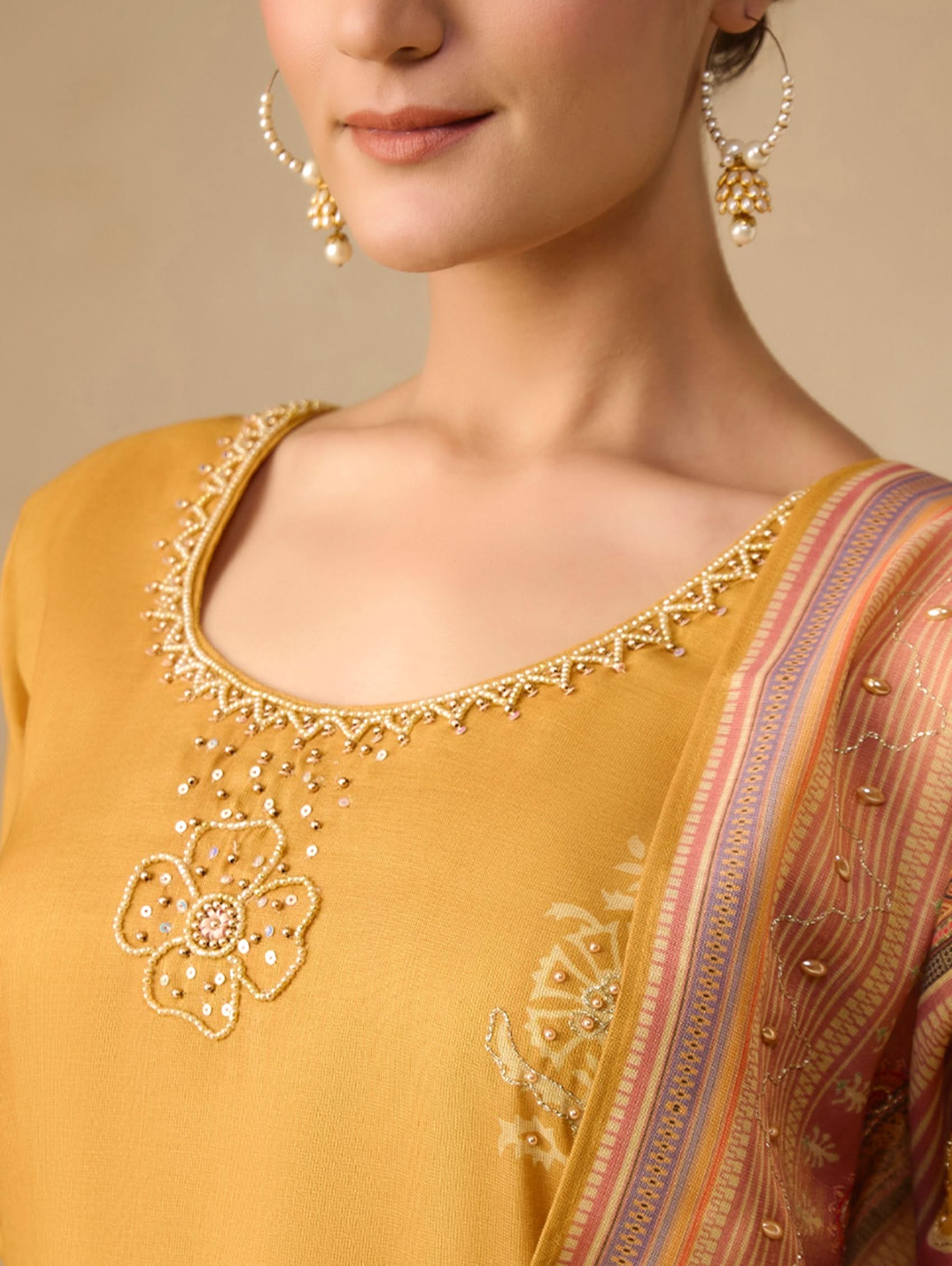 Close-up of a mustard yellow outfit with intricate embroidery and a patterned saree.