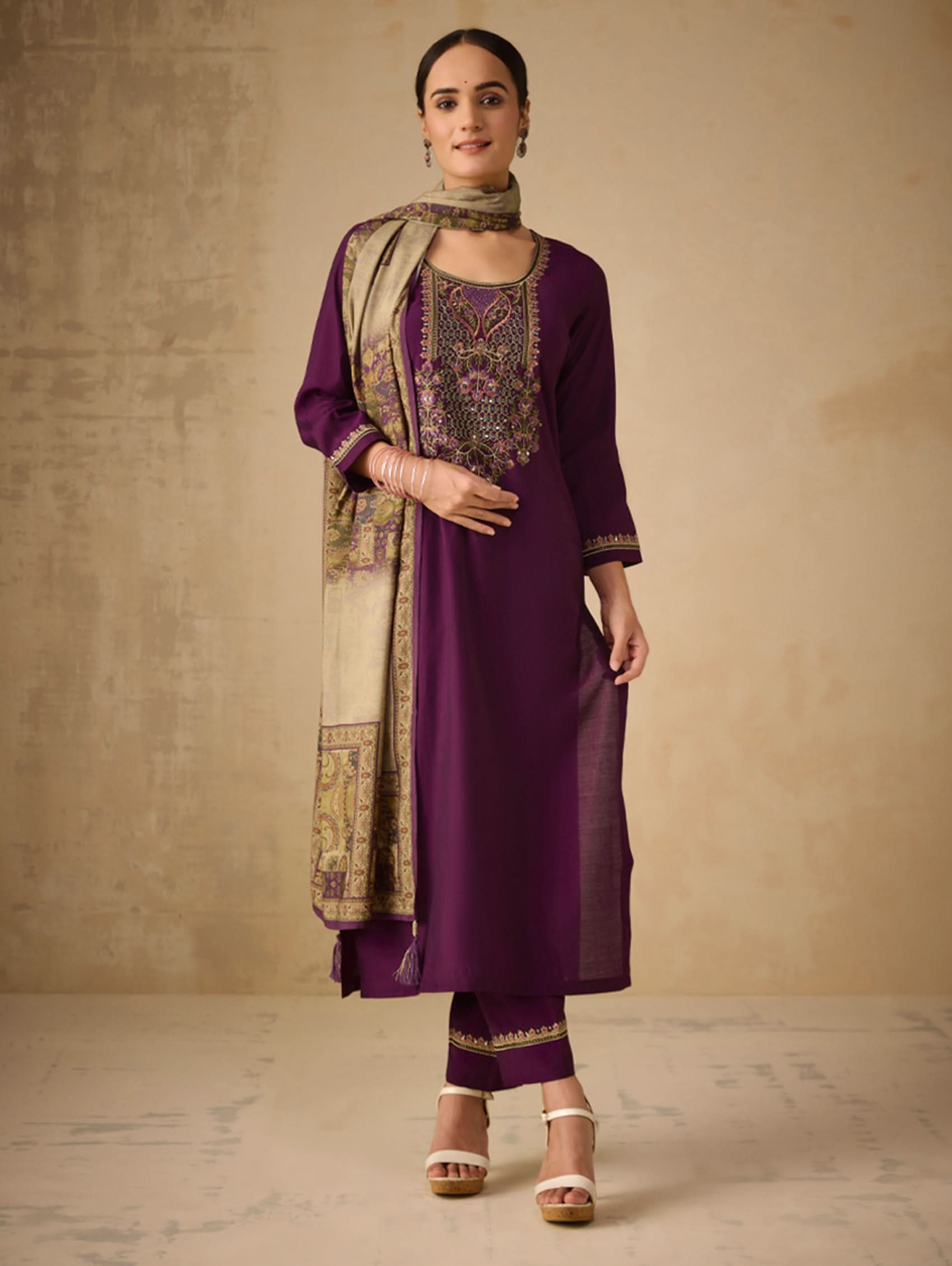 Woman wearing a purple traditional outfit with gold embroidery against a beige background