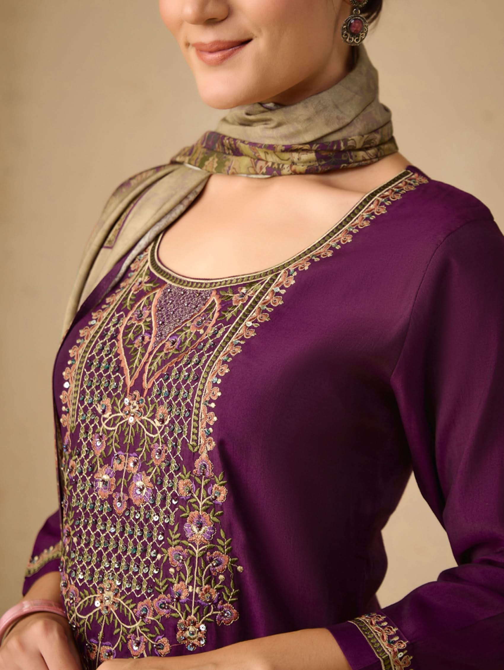 Woman wearing a purple embroidered top with a beige scarf on a beige background