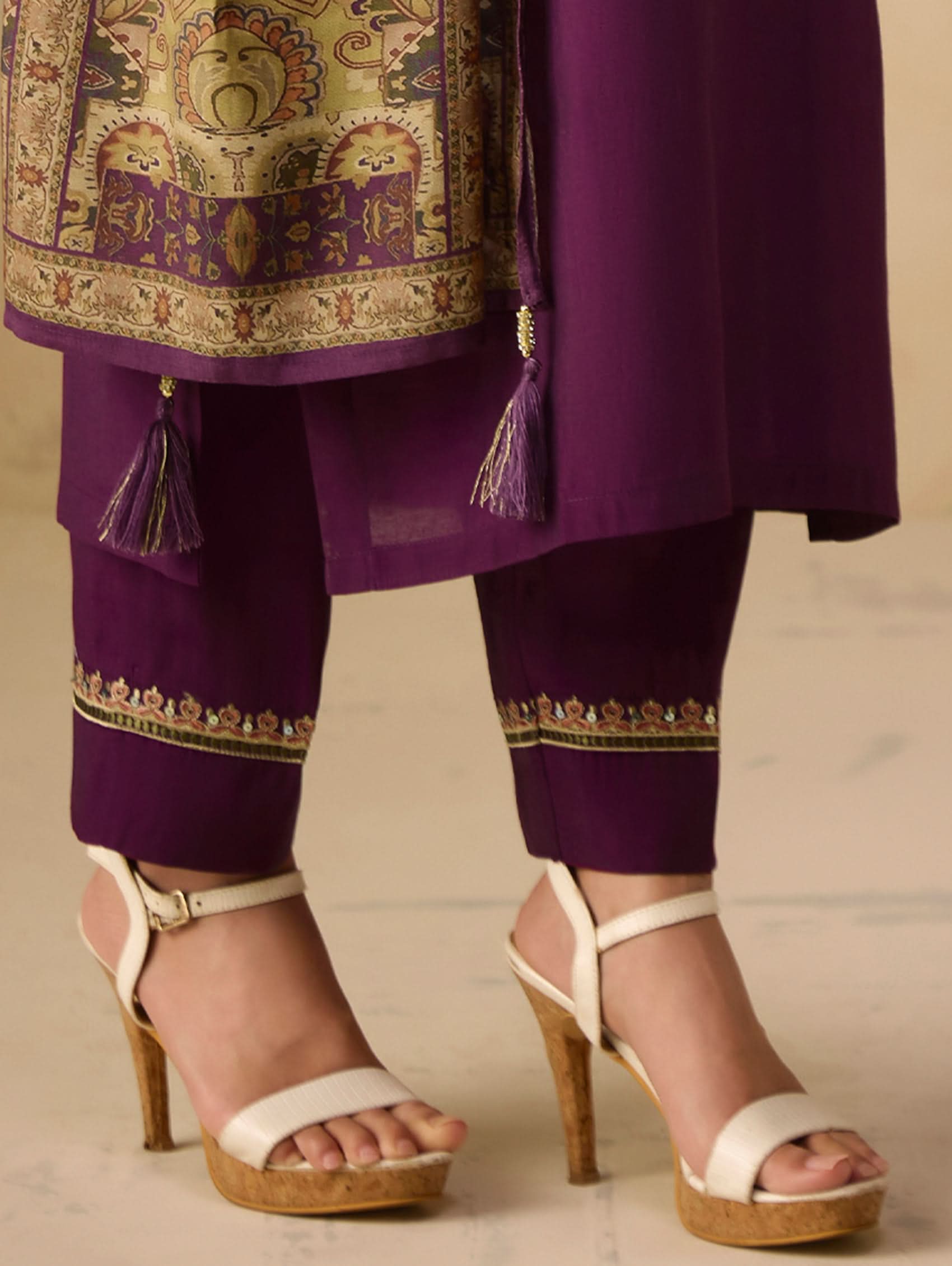 Purple traditional outfit with gold embroidery and white sandals on a beige background