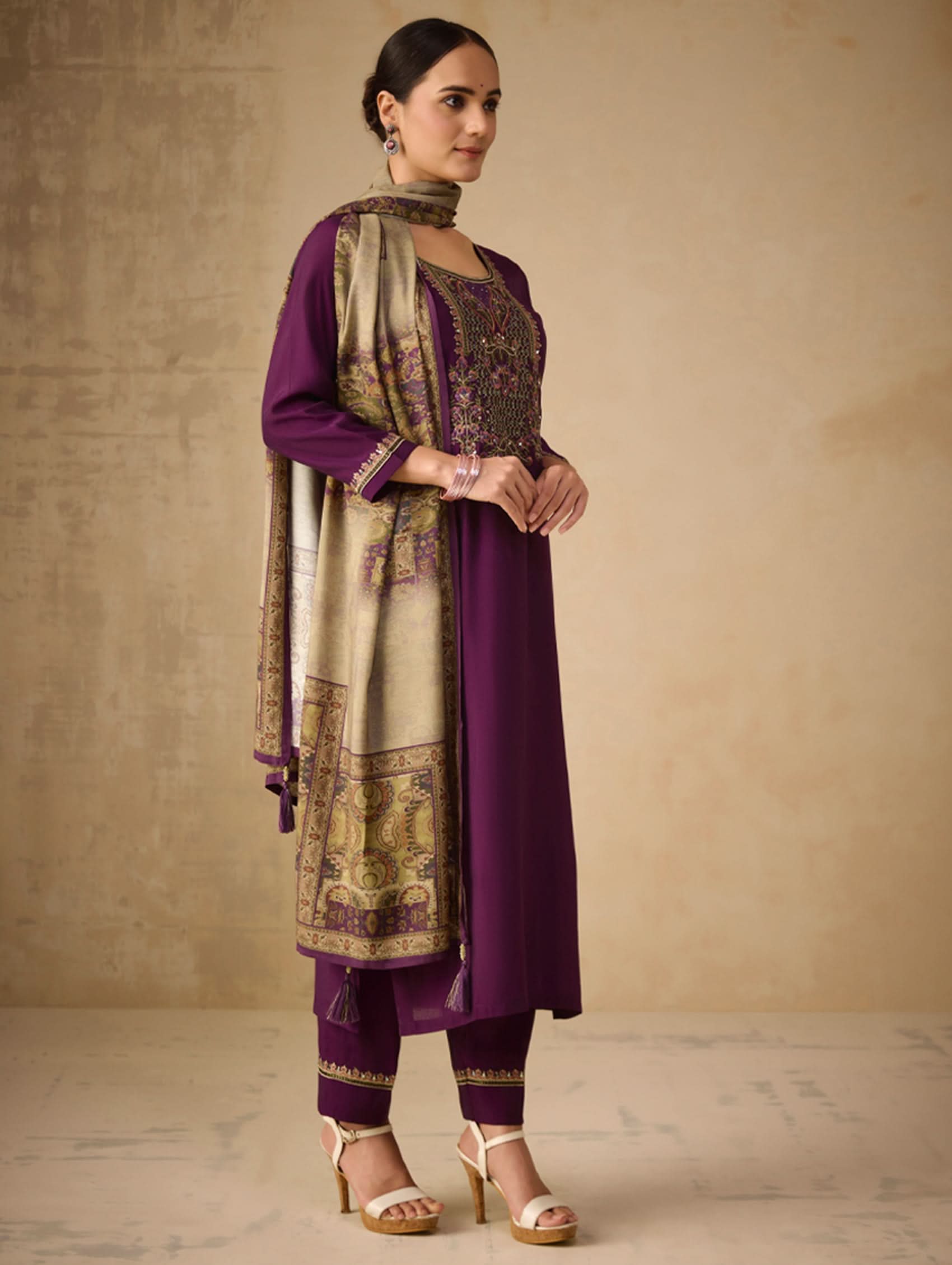 Woman wearing a traditional outfit with a purple and gold theme against a beige background