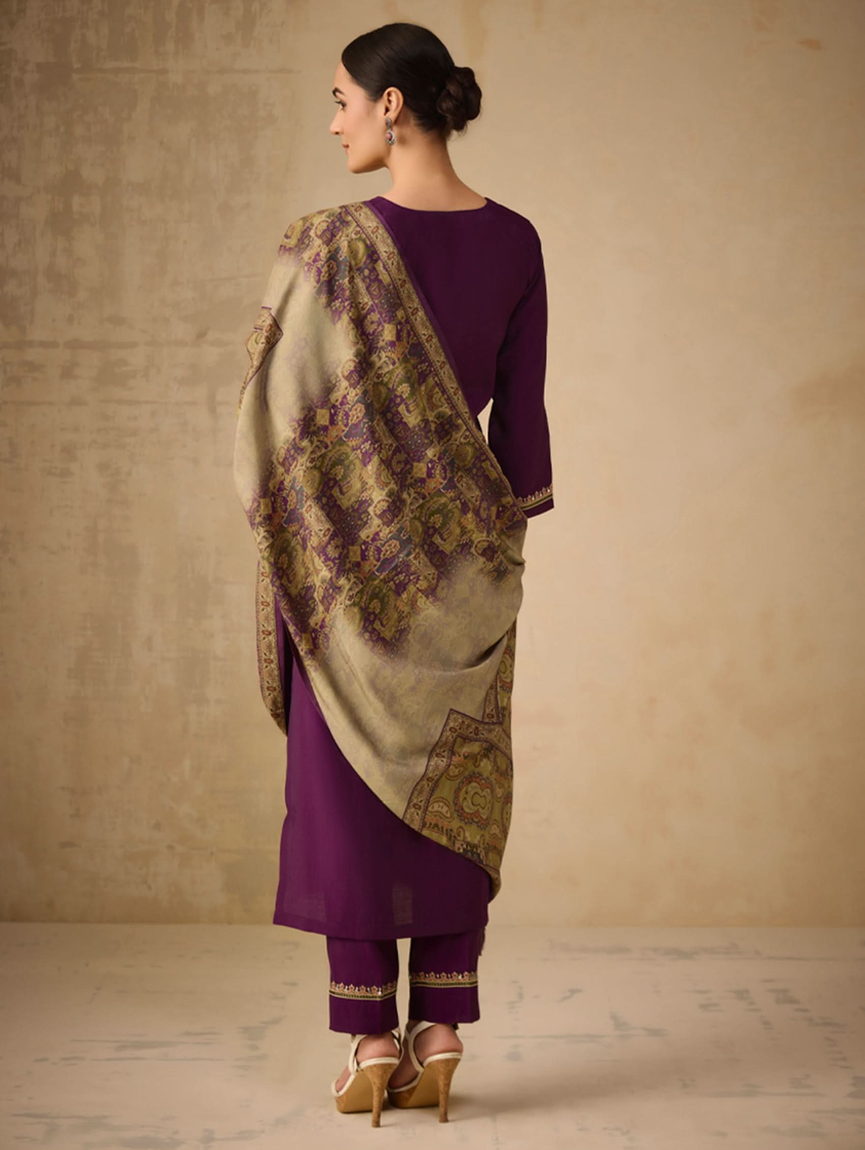 Woman wearing a purple outfit with a beige shawl against a beige background
