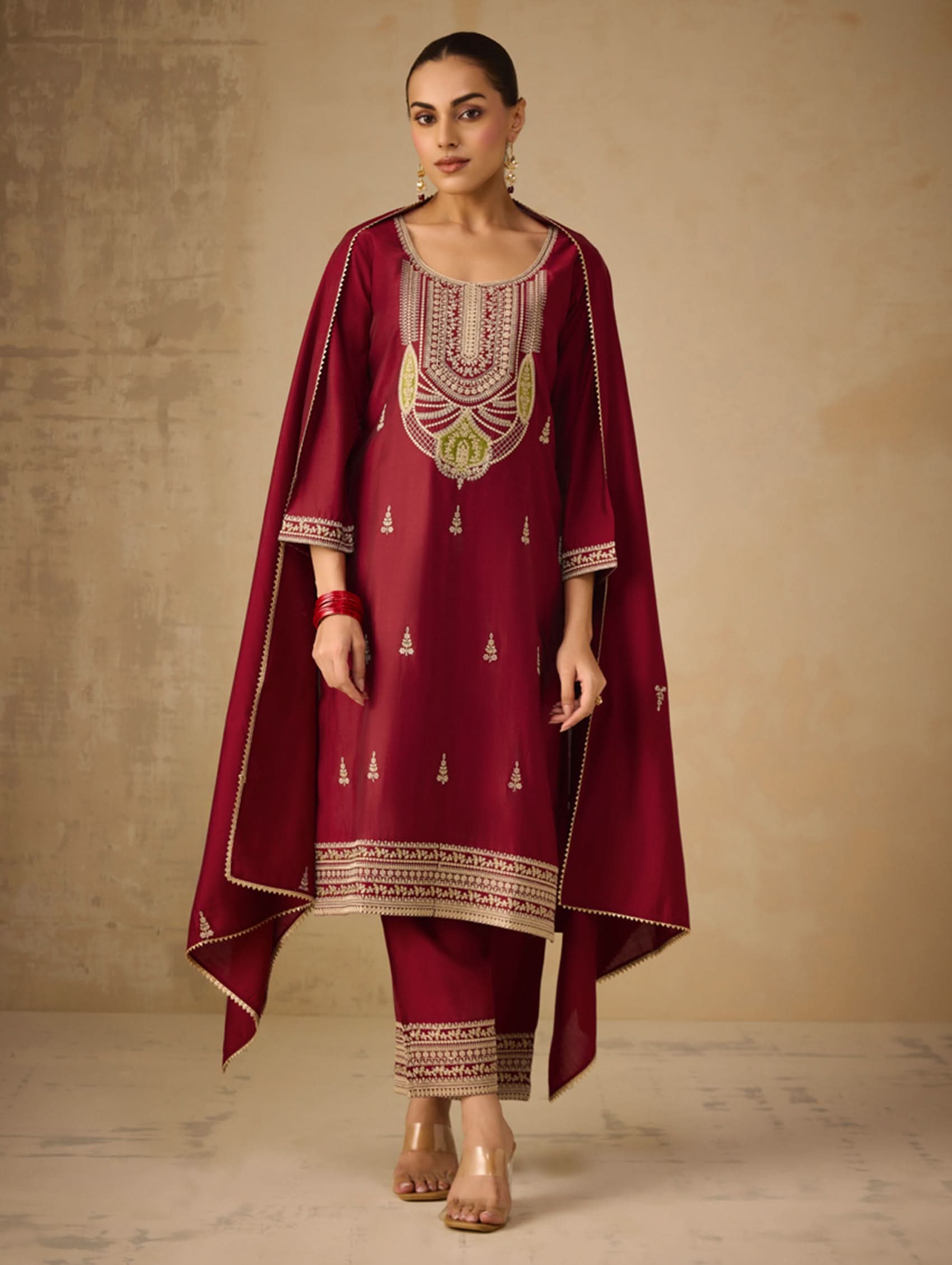 Woman wearing a maroon traditional outfit with embroidery against a beige background