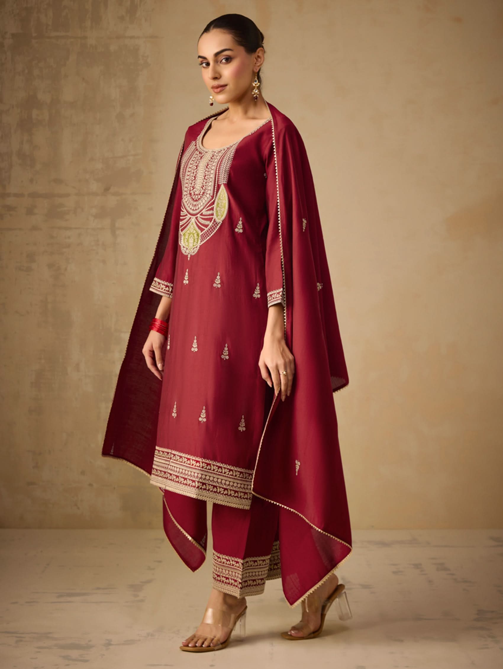 Woman wearing a maroon traditional outfit with embroidery on a beige background