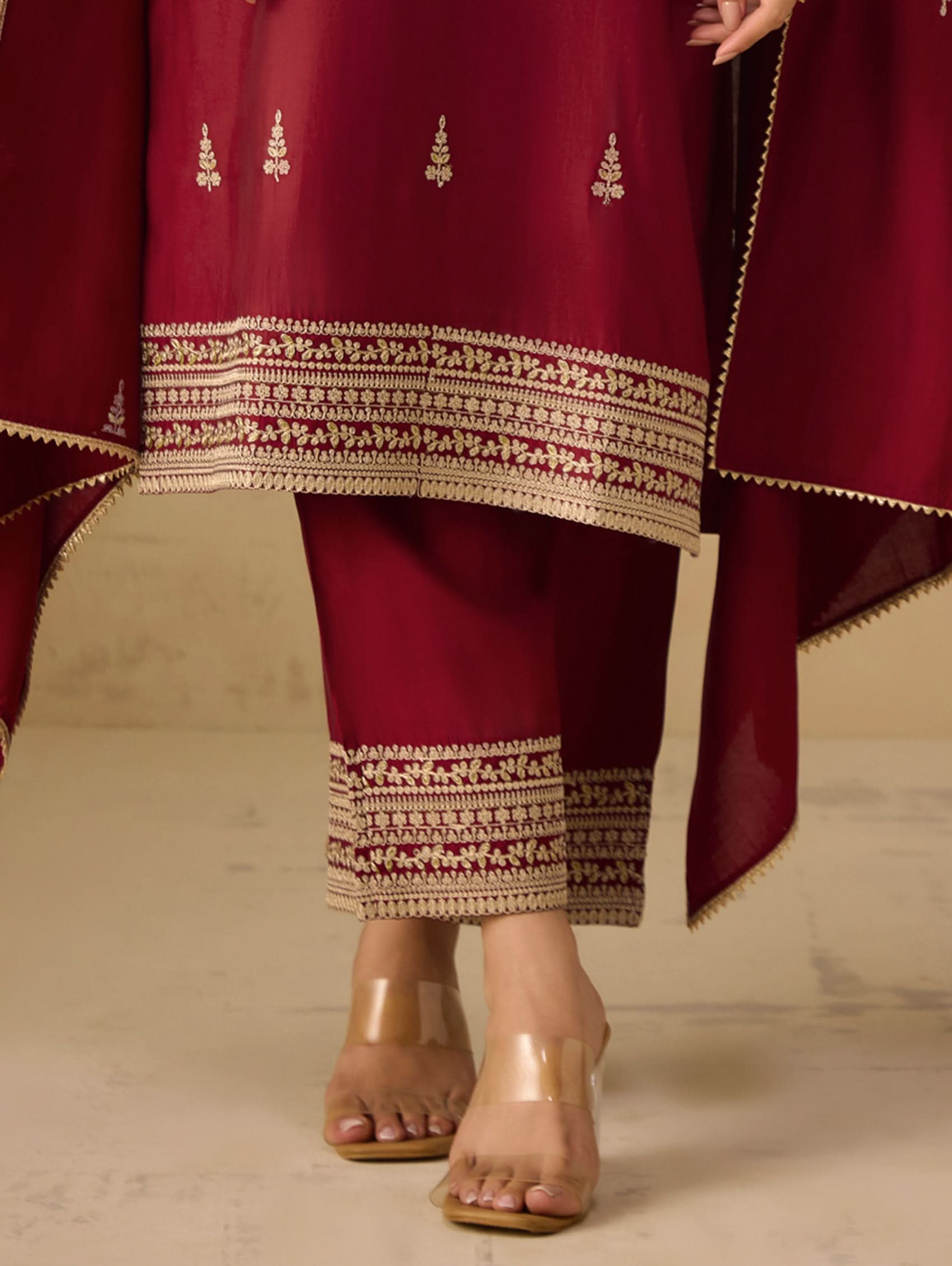 Maroon traditional outfit with gold embroidery on a neutral background