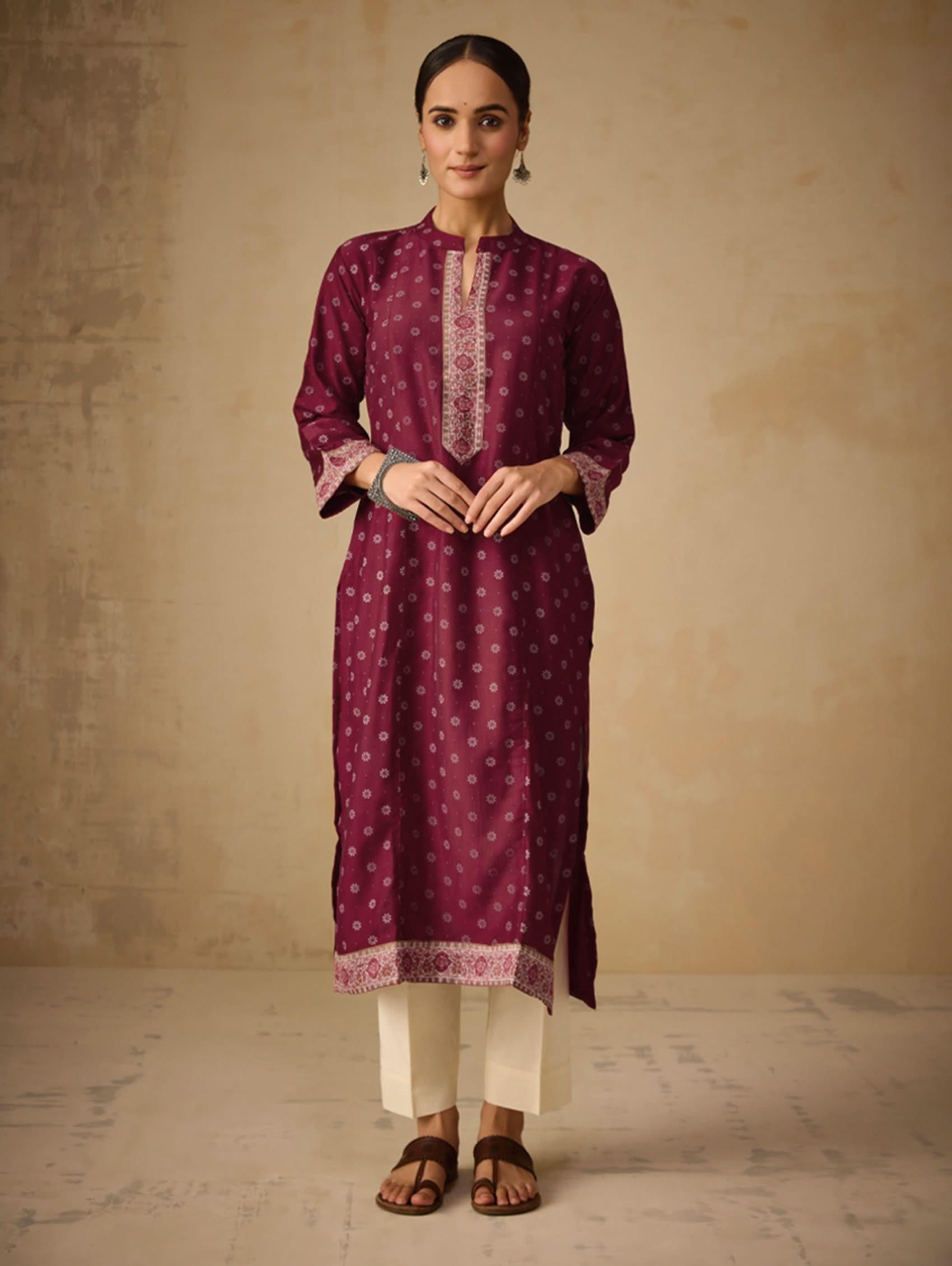 Woman wearing a maroon kurta with white pants against a beige background