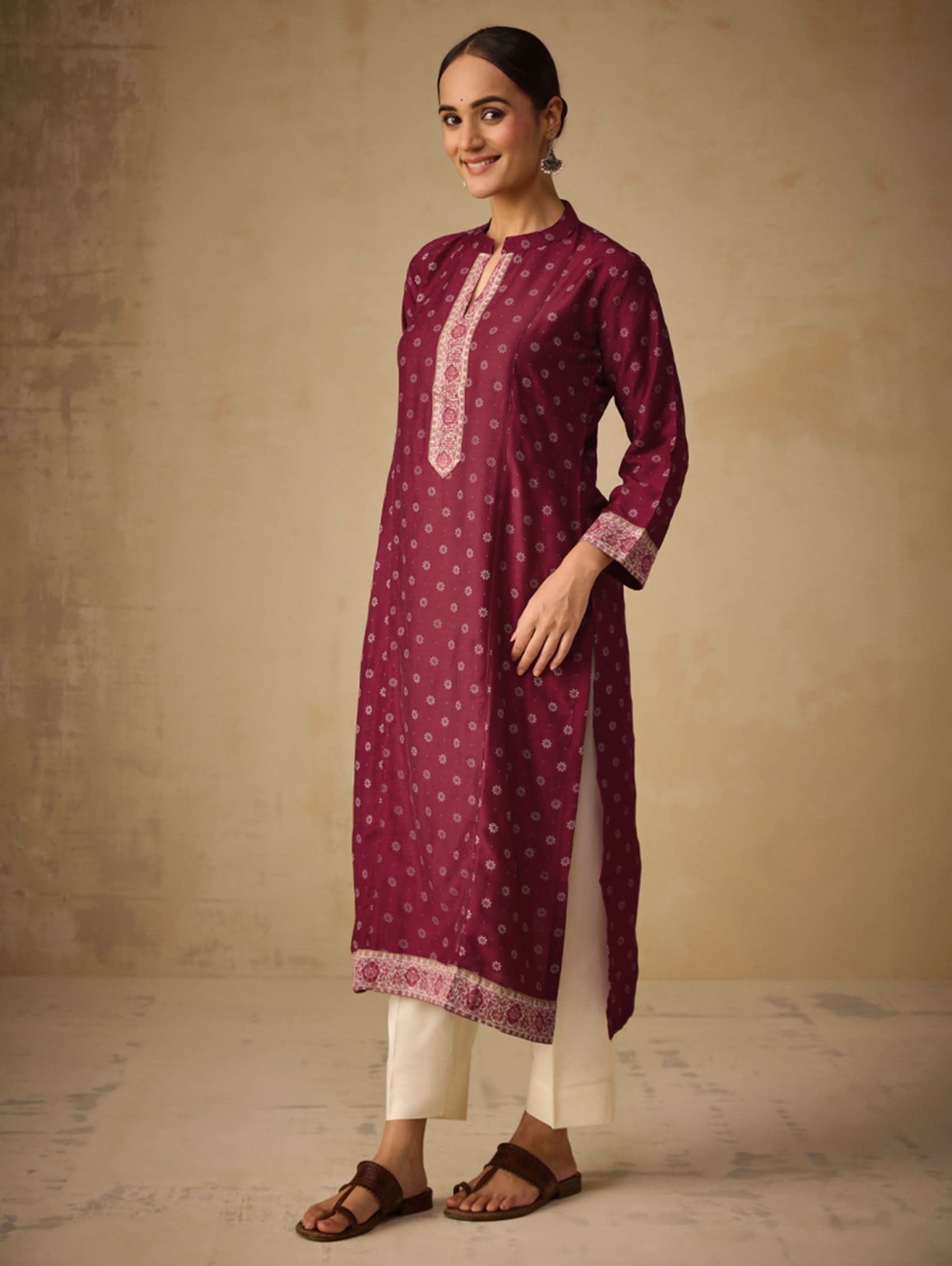 Woman wearing a maroon kurta with white patterns against a beige background