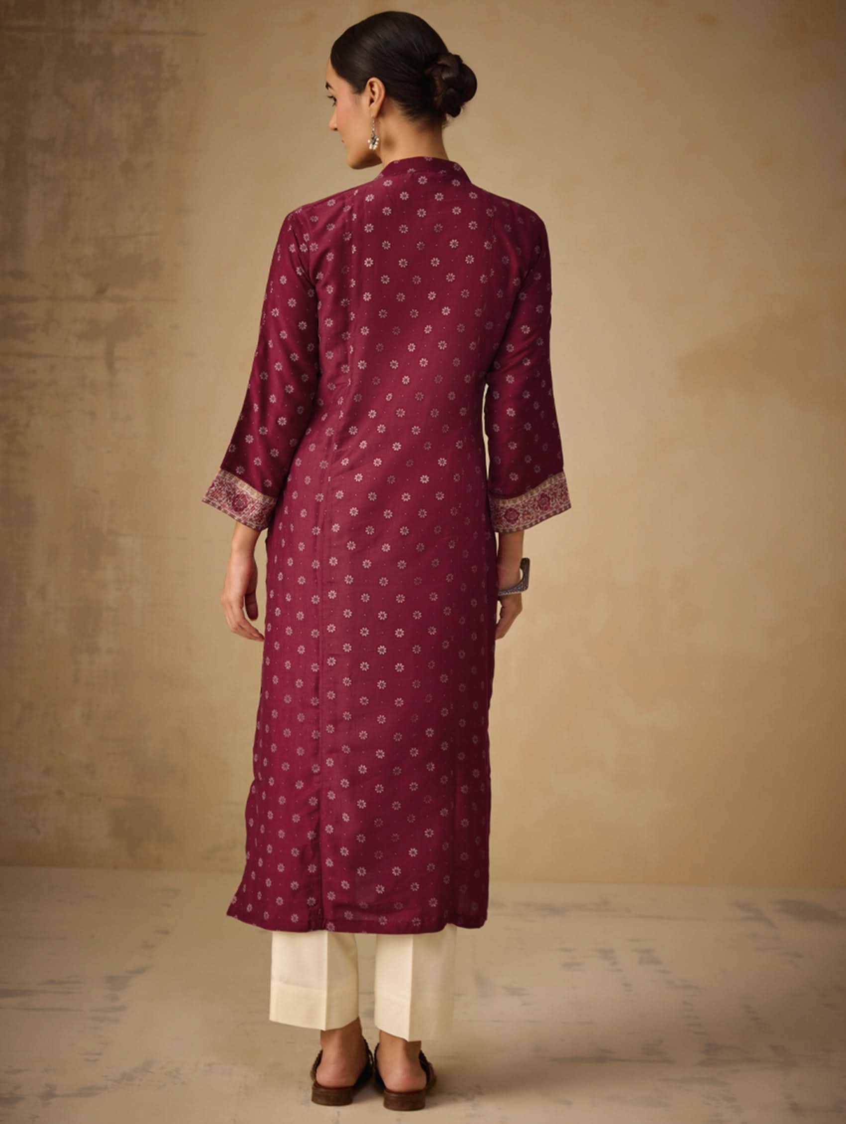 Woman wearing a maroon kurta with white patterns and white pants against a beige background